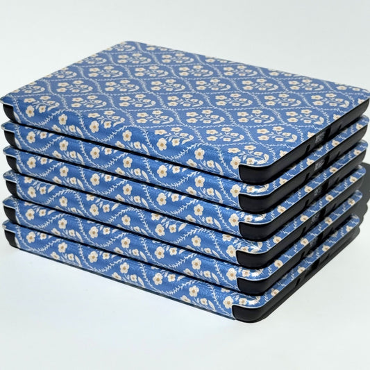 Stack of Bluebell blue floral Kindle cases showing the slim cream-flower design from the side