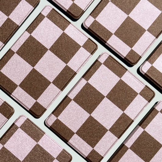 Aesthetic flatlay of She's Checked In Kindle cases in a diamond grid showing pink and brown checkerboard