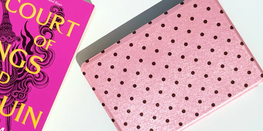 A pink polka dot Kindle case resting beside a hot pink A Court of Wings and Ruin paperback.