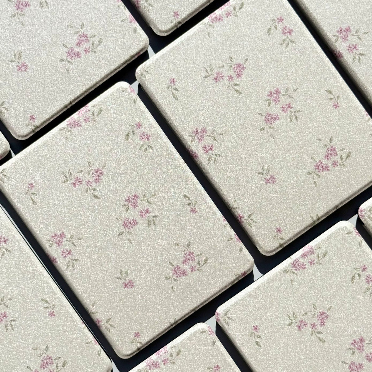 Blooming Kindle cases laid flat, a soft pink ditsy floral on shimmering cream