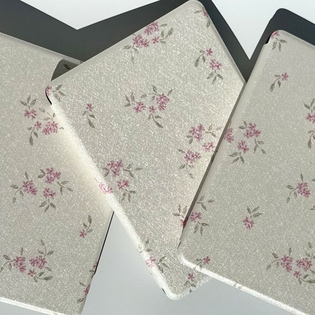 Three Blooming Kindle cases fanned together, pink blossoms and sage leaves on ivory