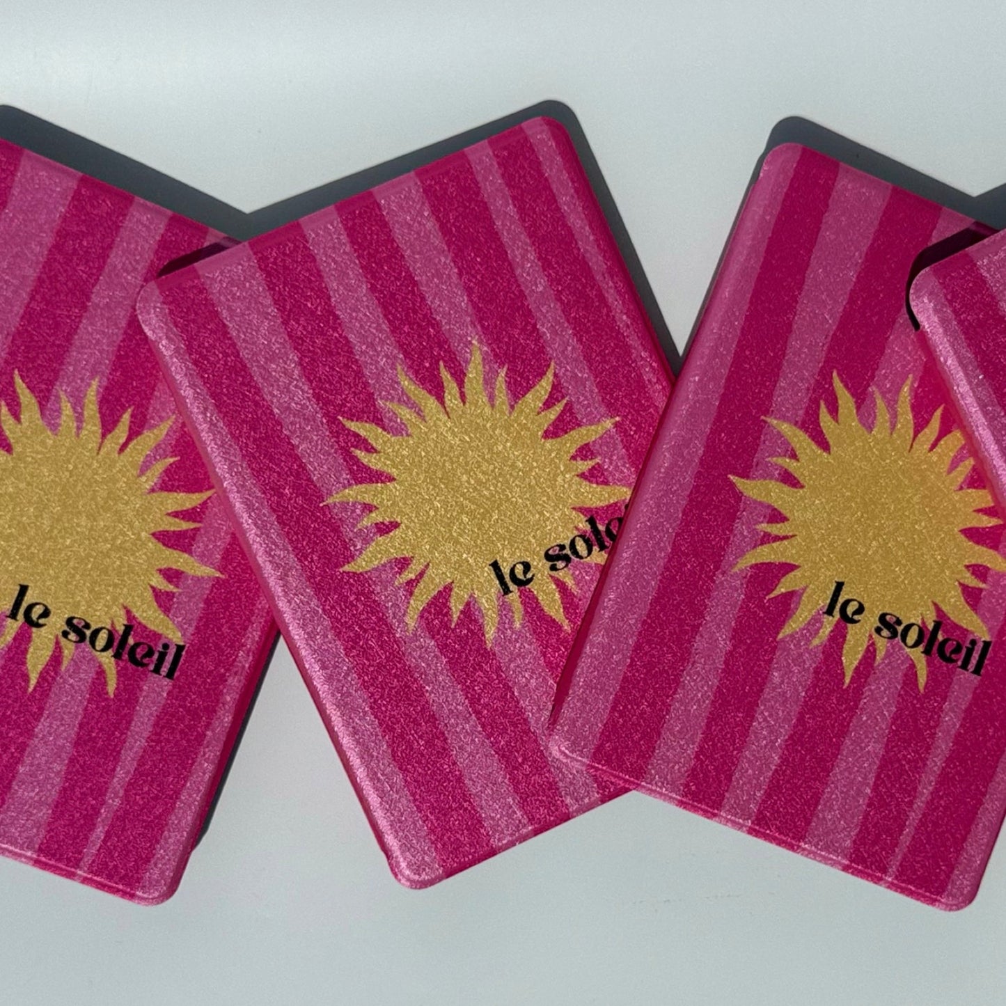 Front view of overlapping Le Soleil pink striped Kindle cases with gold sun
