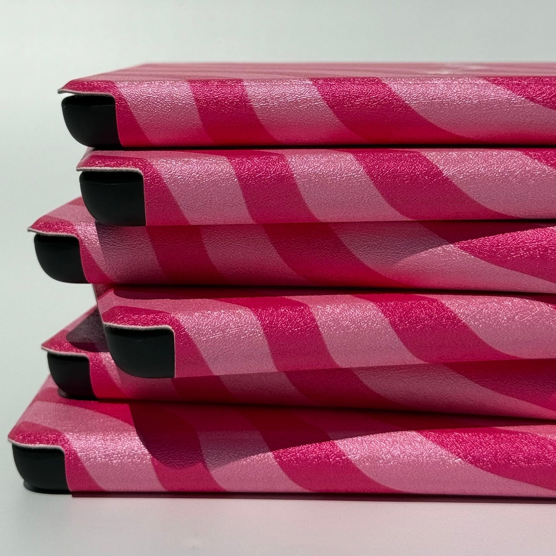 Close-up side stack of Shhh I'm Reading pink wavy Kindle cases