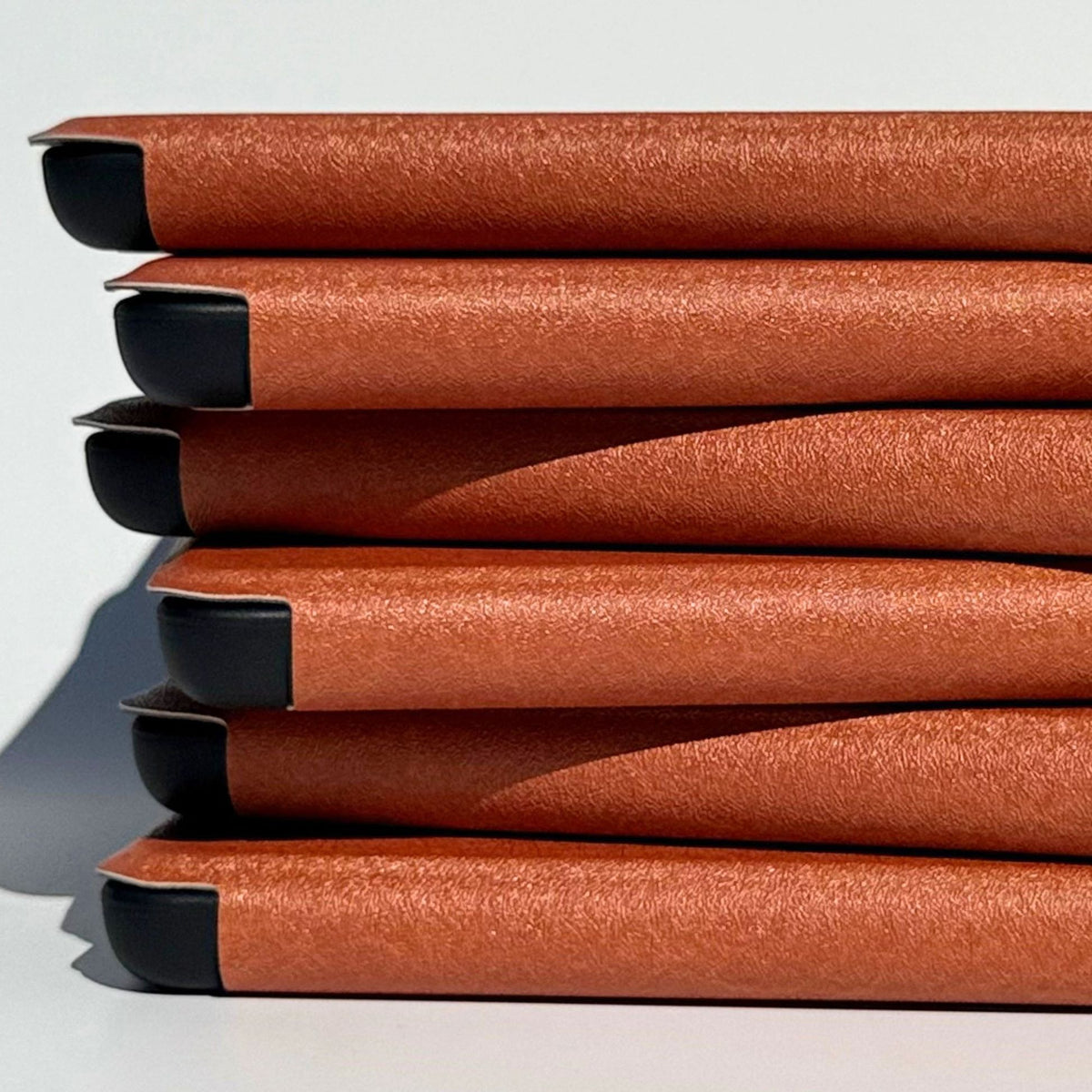 Close stack of A Thousand Lives Kindle cases showing the tan vegan leather spine