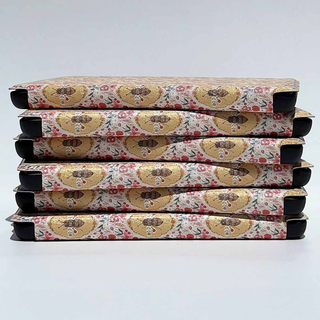 Stack of The Beekeeper's Garden Kindle cases showing vintage golden bee and wildflower pattern — aesthetic floral Kindle case