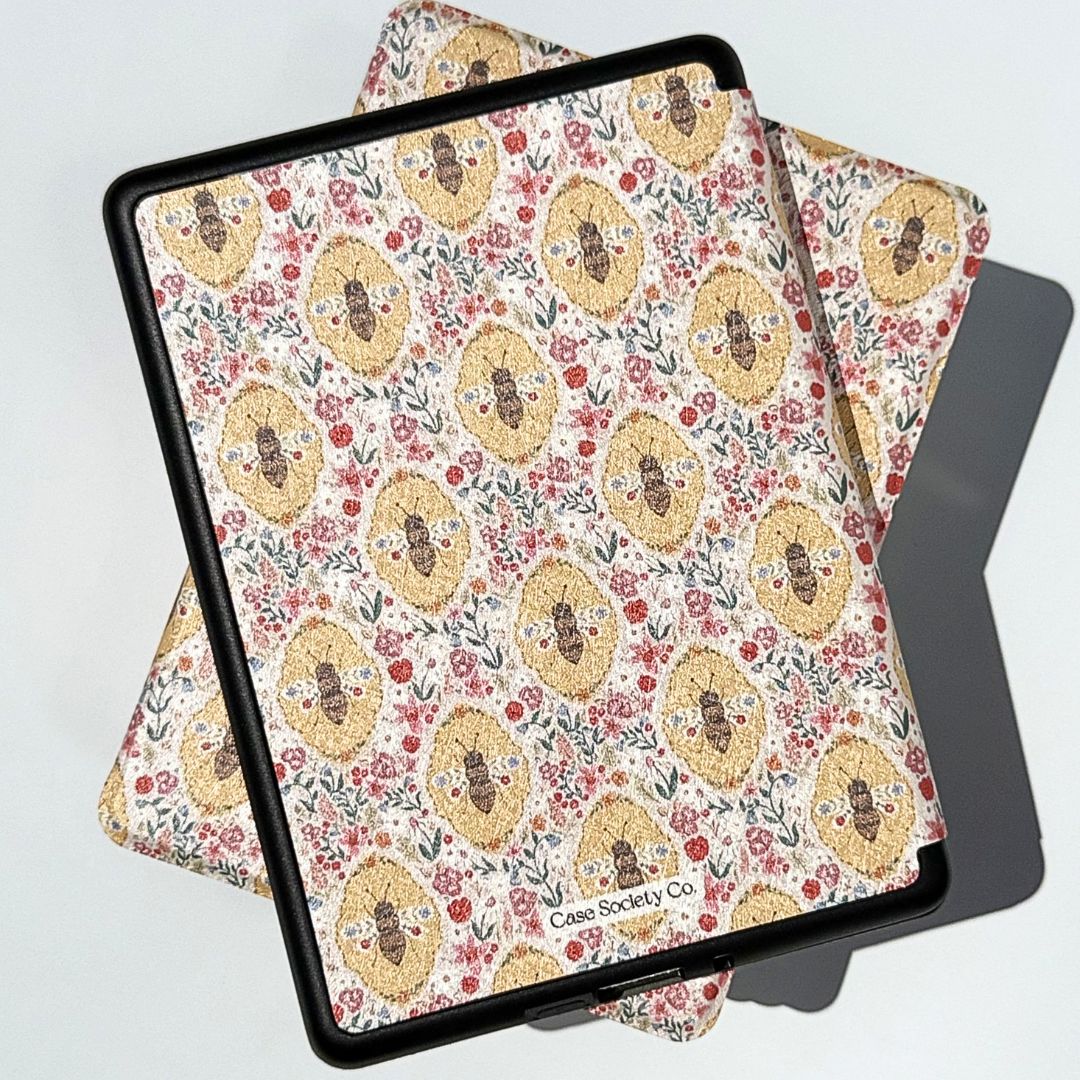Beekeeper's Garden Kindle cases stacked showing golden bee medallions and pink wildflowers — vintage floral Kindle case
