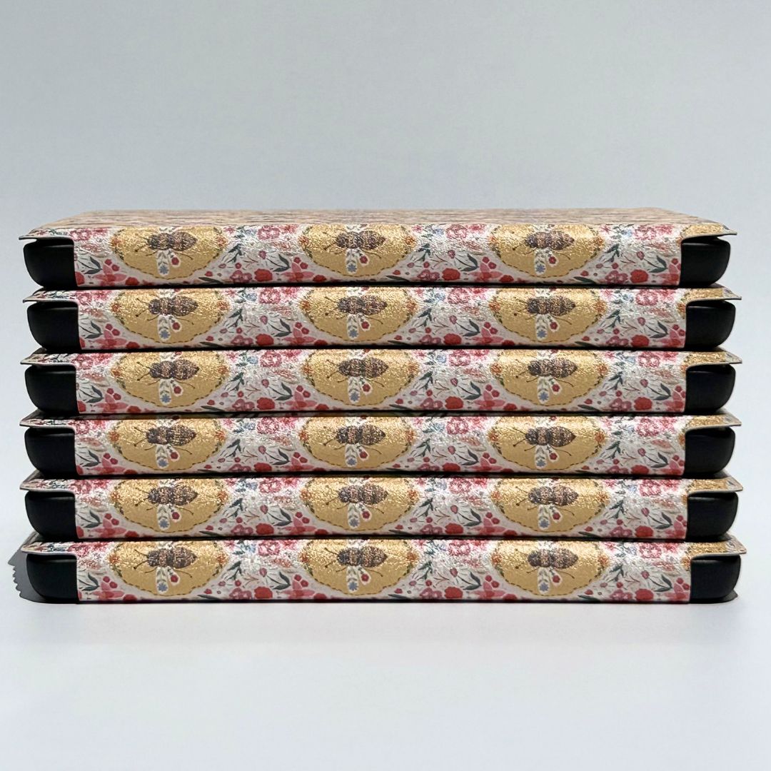 Beekeeper's Garden Kindle cases stacked showing golden bee medallions and pink wildflowers — vintage floral Kindle case