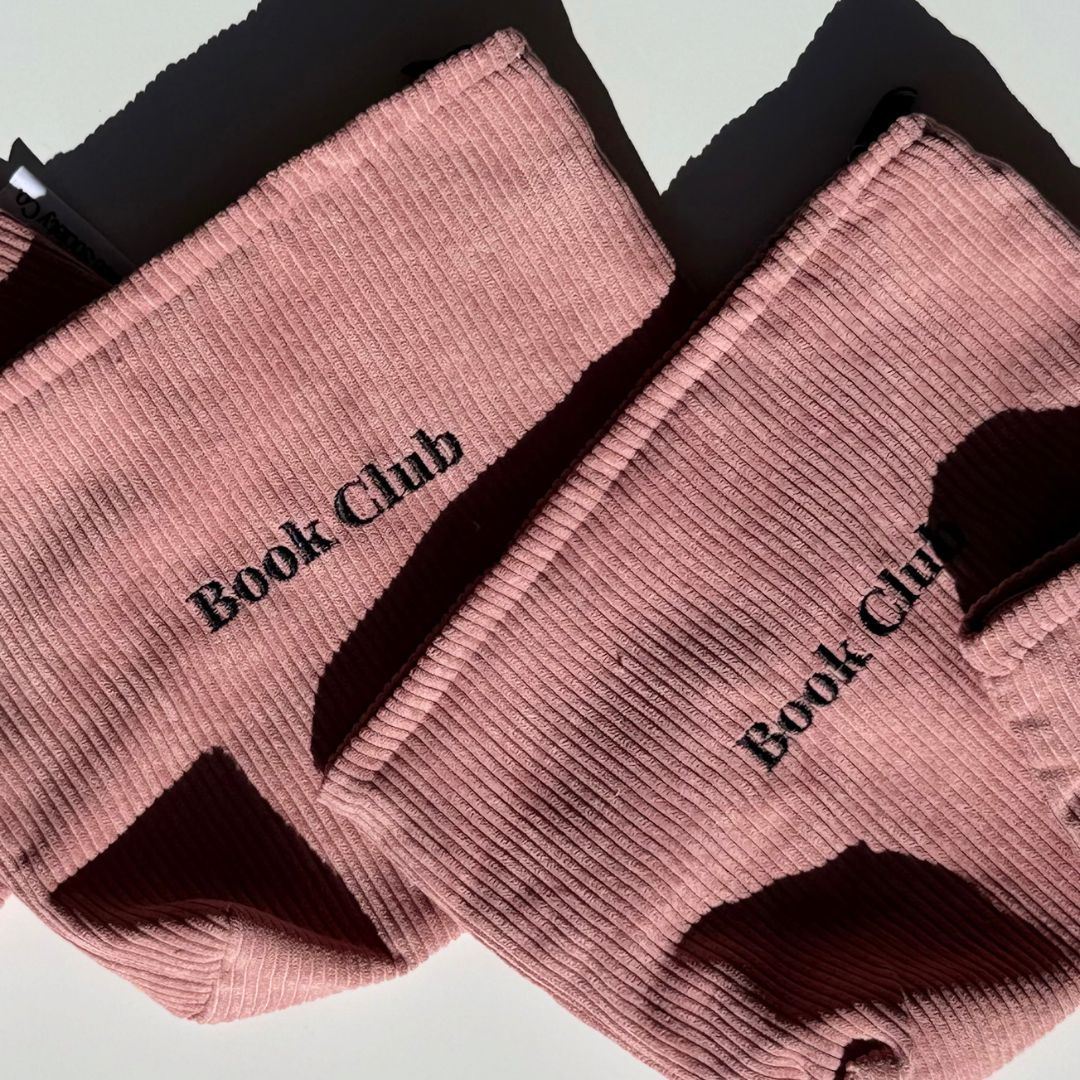 Two blush pink e-reader pouches laid diagonally with Book Club embroidery