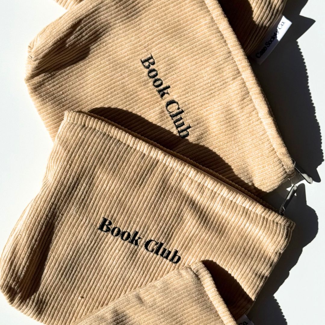 Folded stack of honey Book Club book pouches with woven labels on soft corduroy