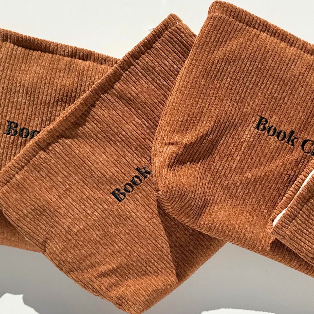 Three mocha corduroy e-reader pouches in a diagonal flatlay with Book Club embroidery