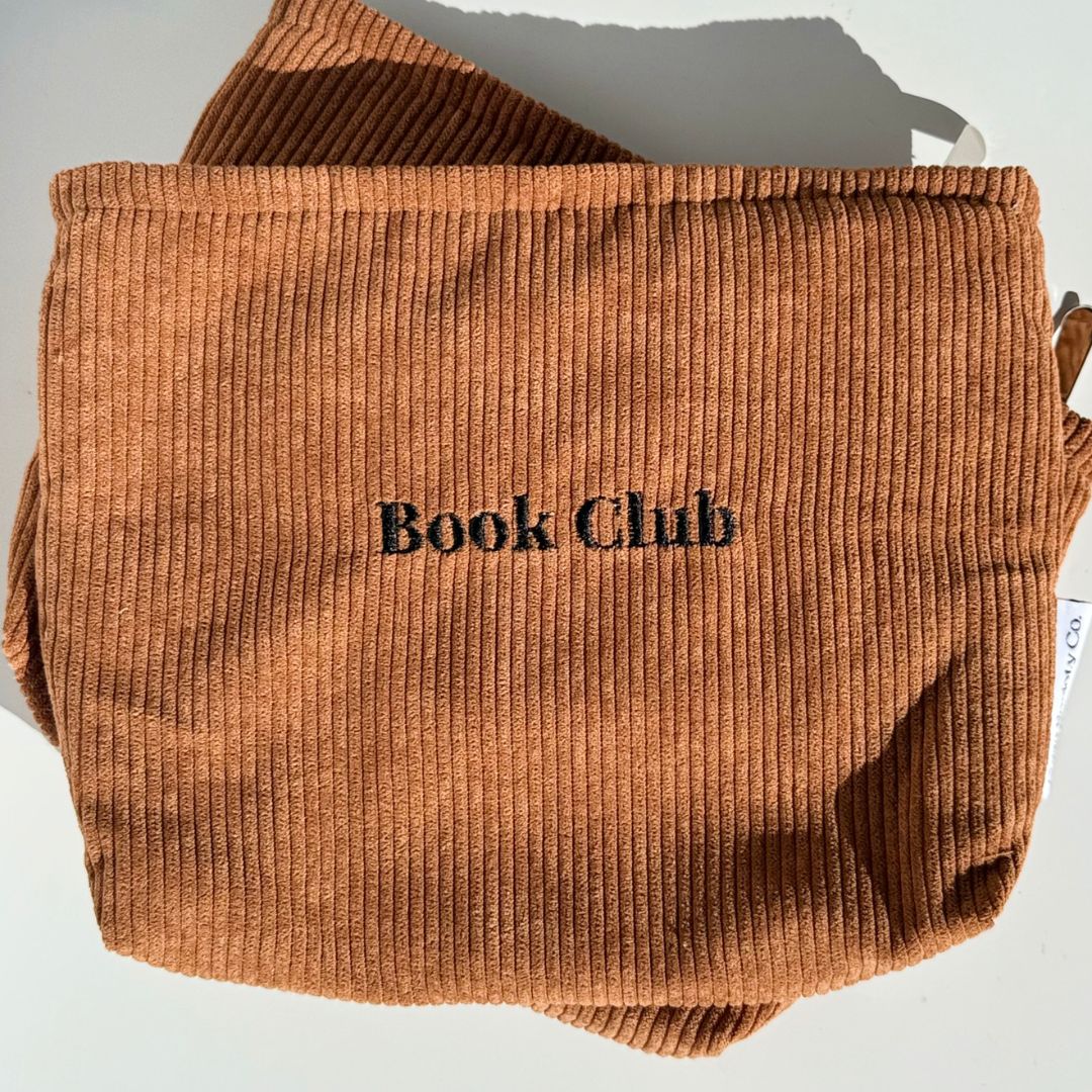 Front of the mocha Book Club kindle pouch with embroidered lettering resting on a second pouch
