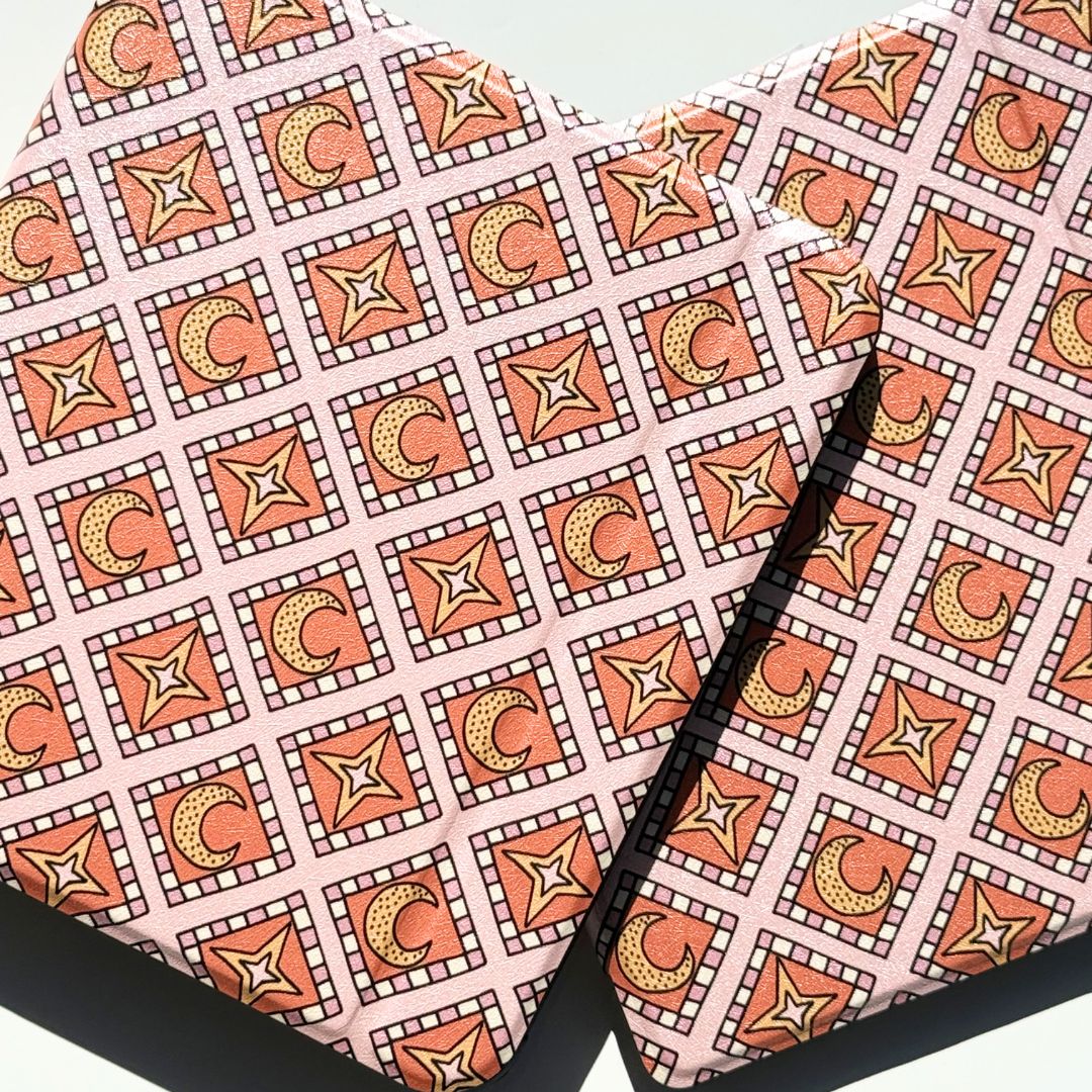 Two Celestia Kobo cases laid flat showing the star and crescent moon mosaic print on blush pink