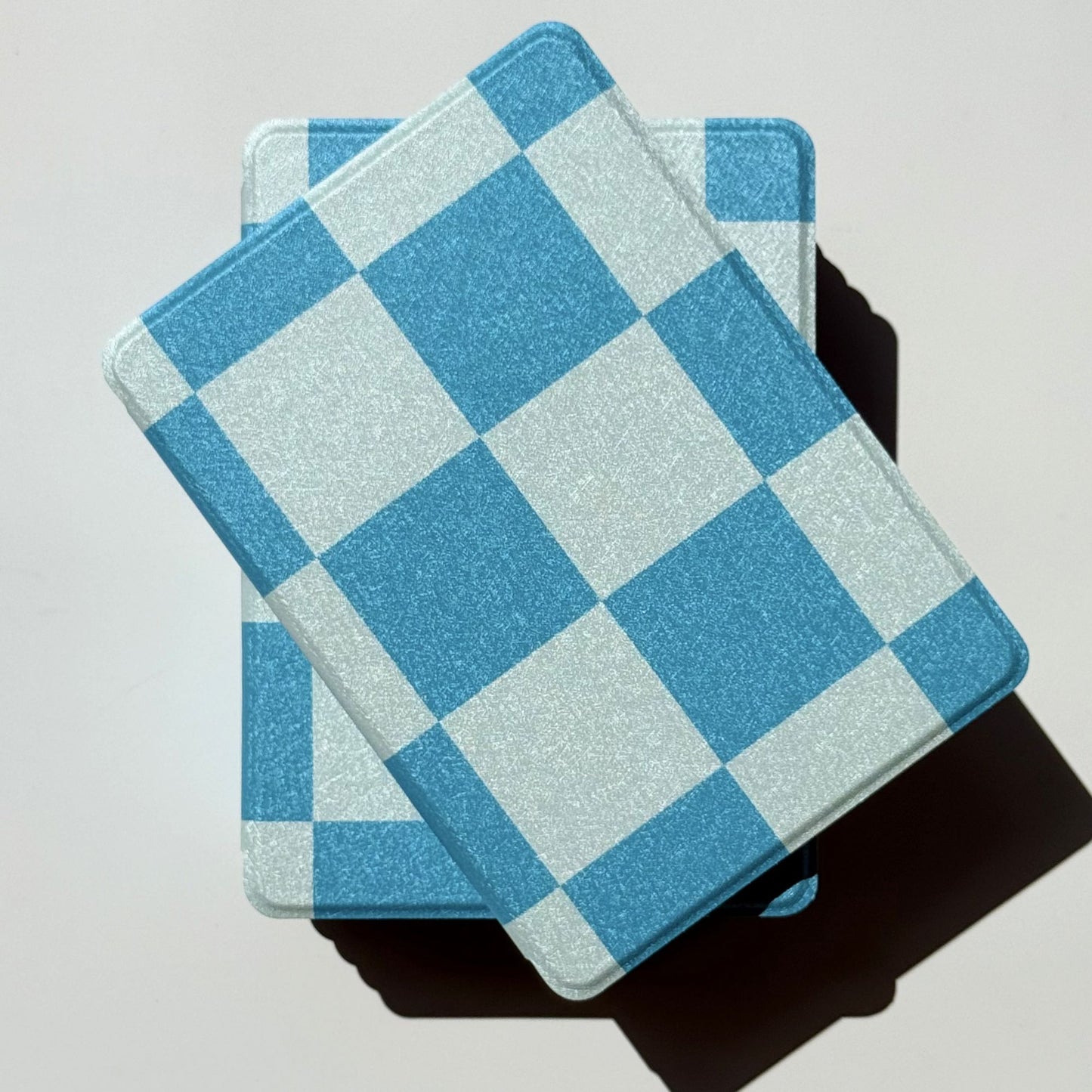 Two blue gingham Kindle cases overlapped in a soft flatlay