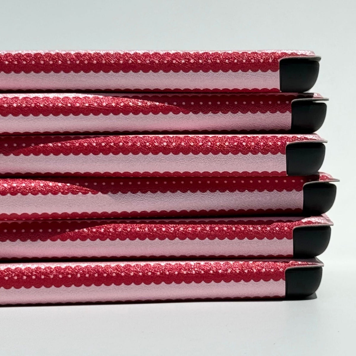 Cherry Ledger Kindle cases stacked edge-on, red scalloped stripes with white pin-dots, Australia