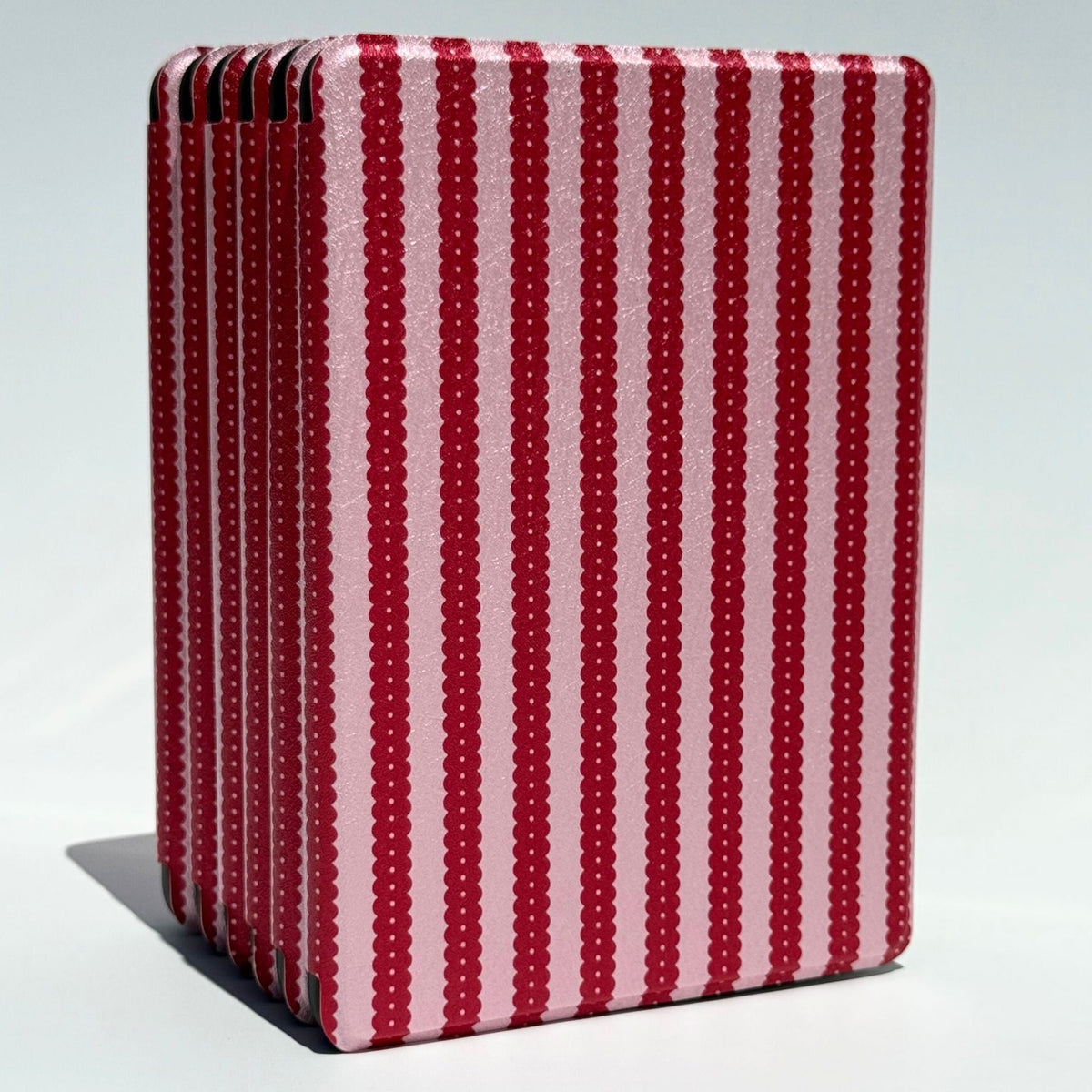 Cherry Ledger Kindle case standing upright, cherry red scalloped stripes on shimmer pink