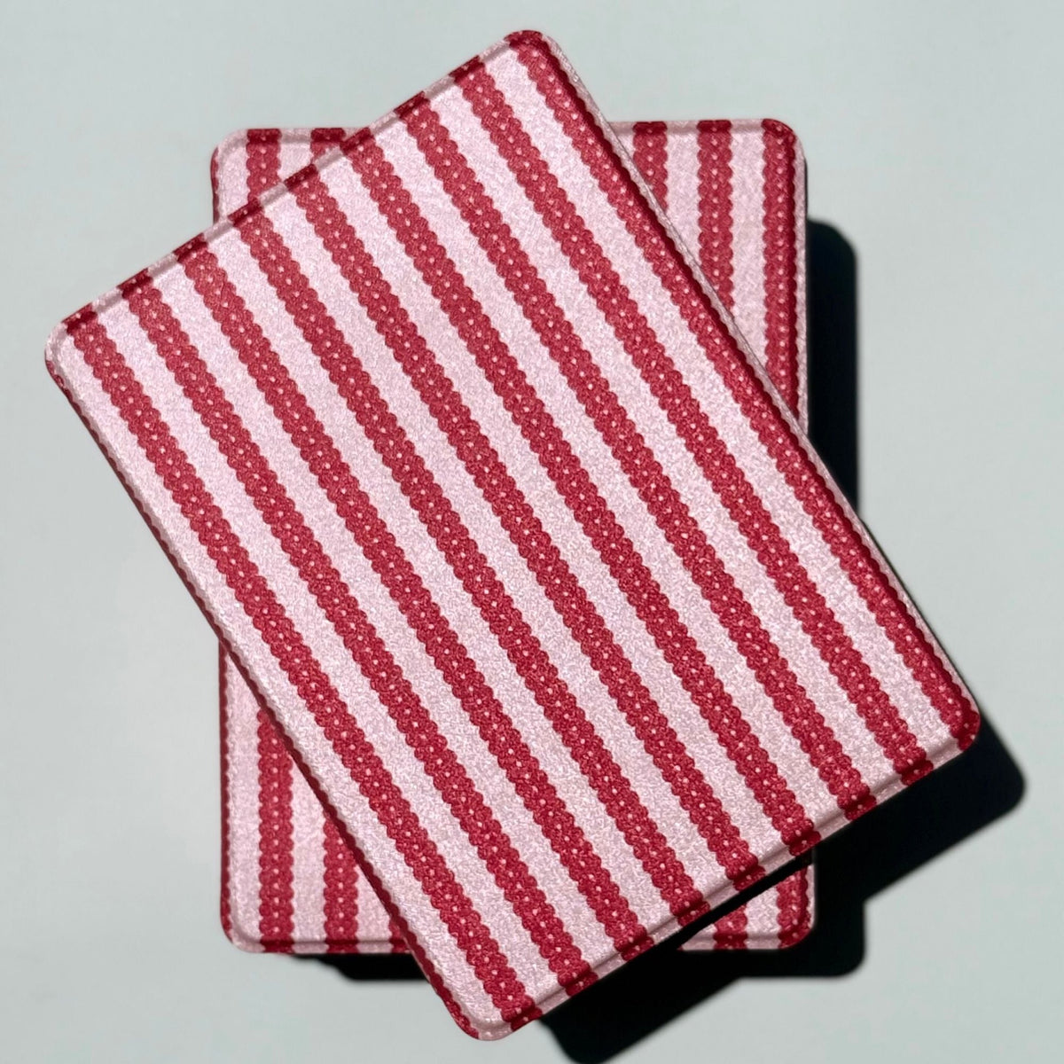 Two Cherry Ledger Kindle cases overlapped in sunlight, red and pink stripes edge to edge