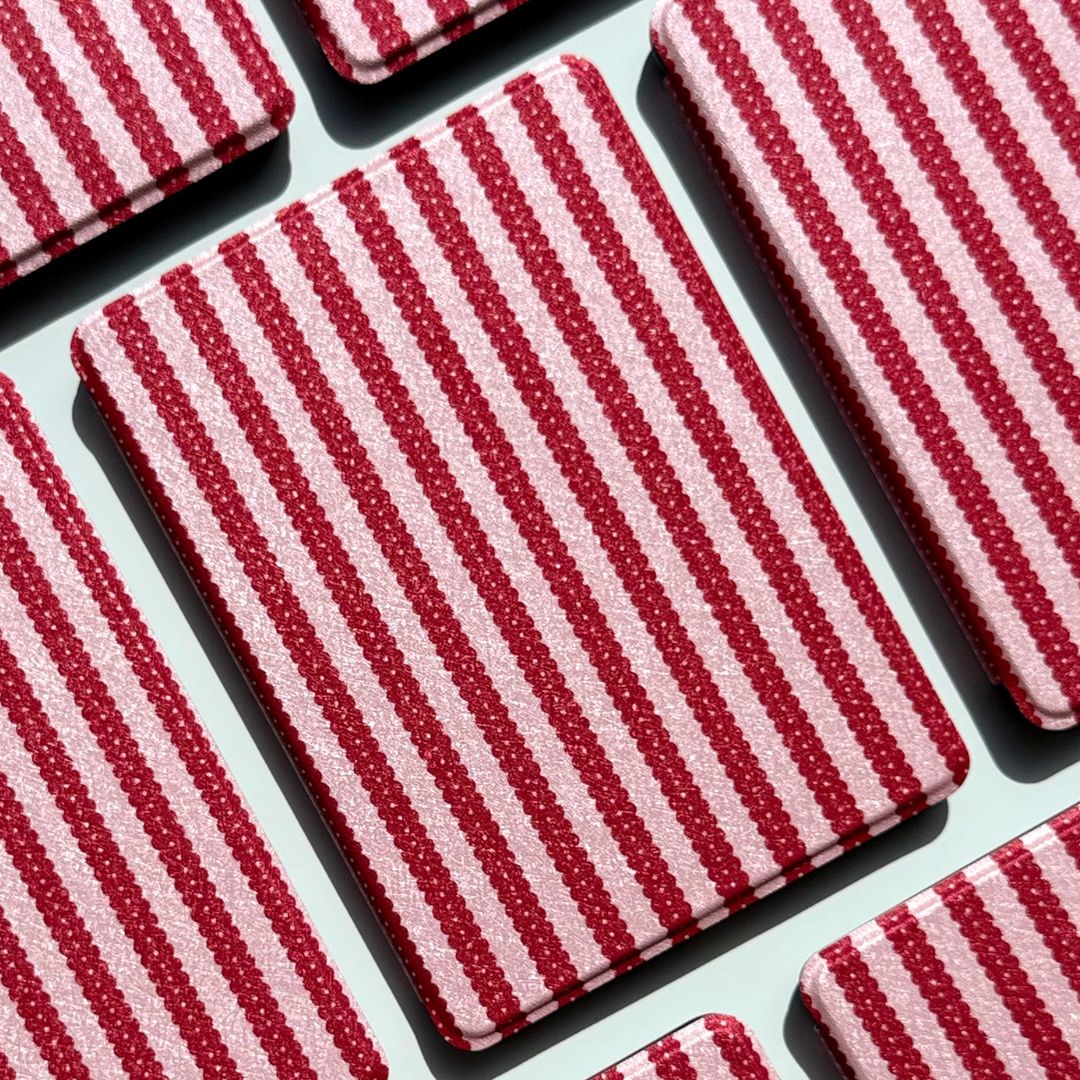 A Cherry Ledger Kindle case centred in a grid of striped cases, red stripes on blush pink.