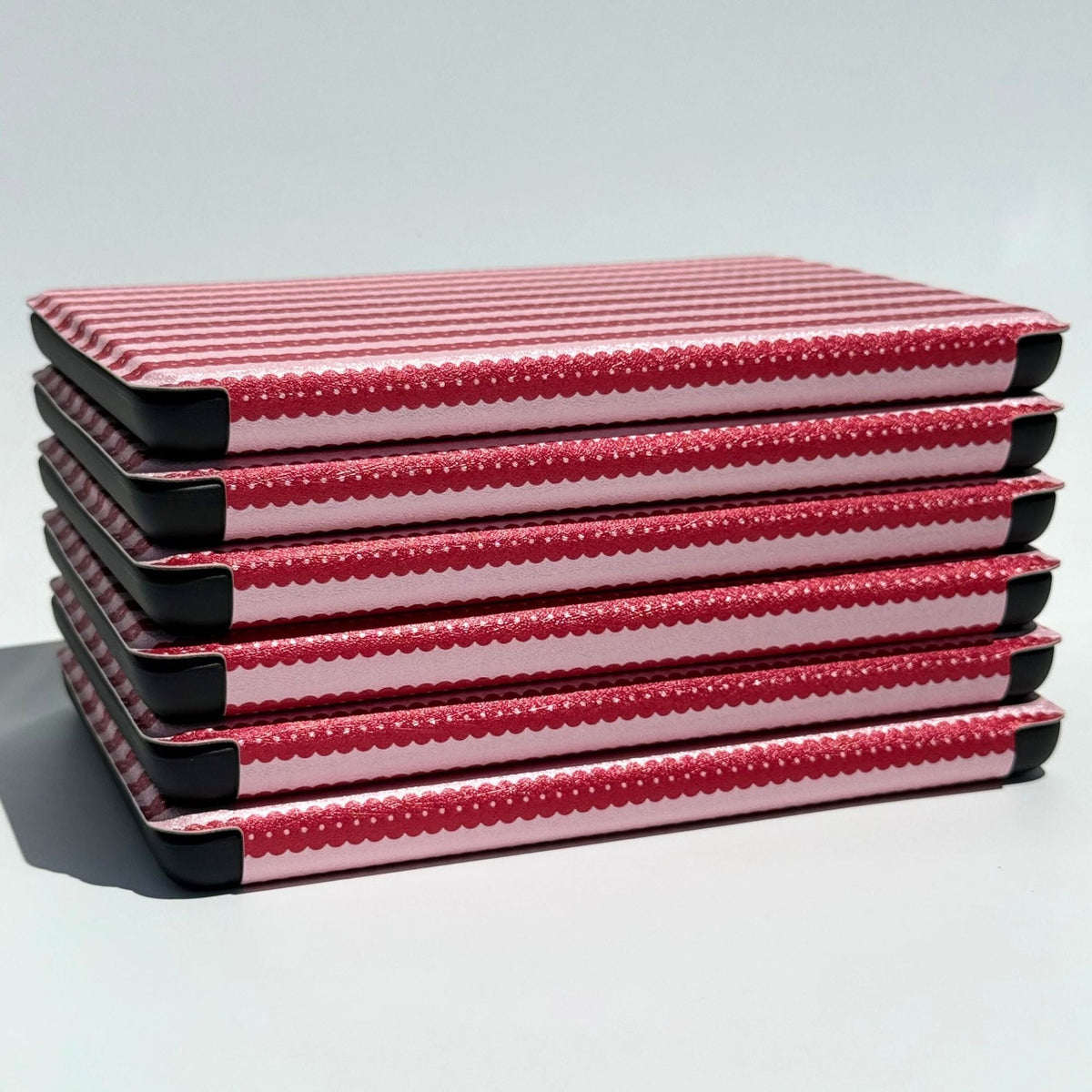 Six Cherry Ledger Kindle cases stacked at an angle, striped spines catching the light