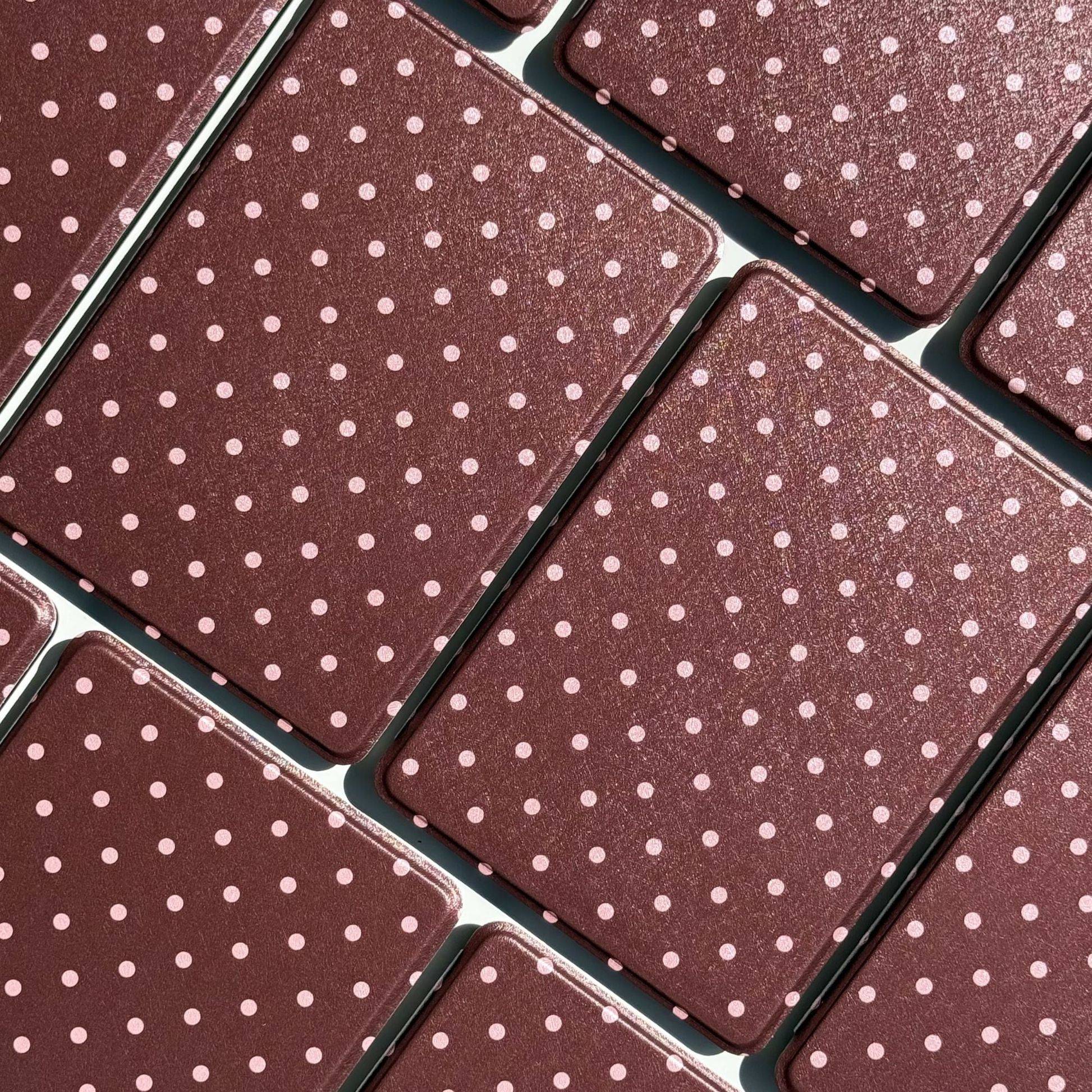 Flatlay of Cocoa Kiss Kindle cases in chocolate brown with pink polka dots, laid edge to edge in sunlight