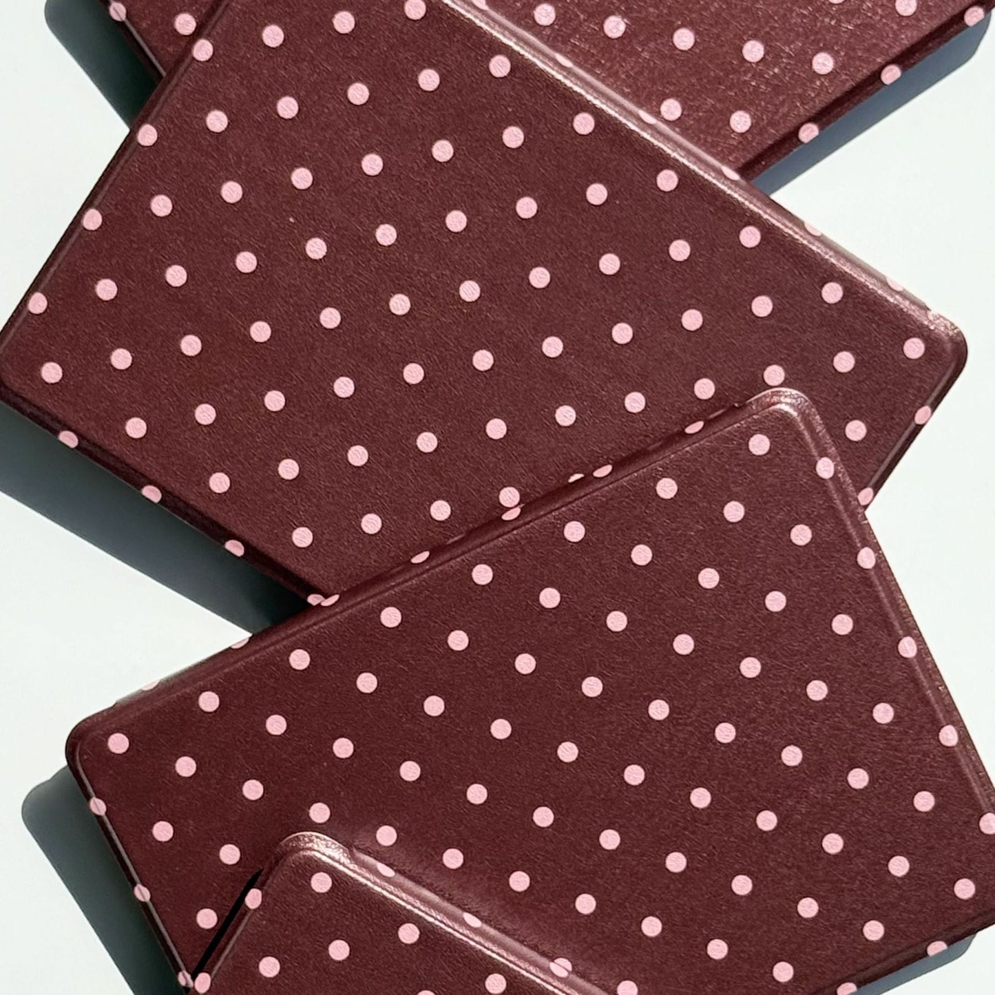 Close-up of overlapping Cocoa Kiss Kindle cases showing the soft pink polka dot print and slim profile