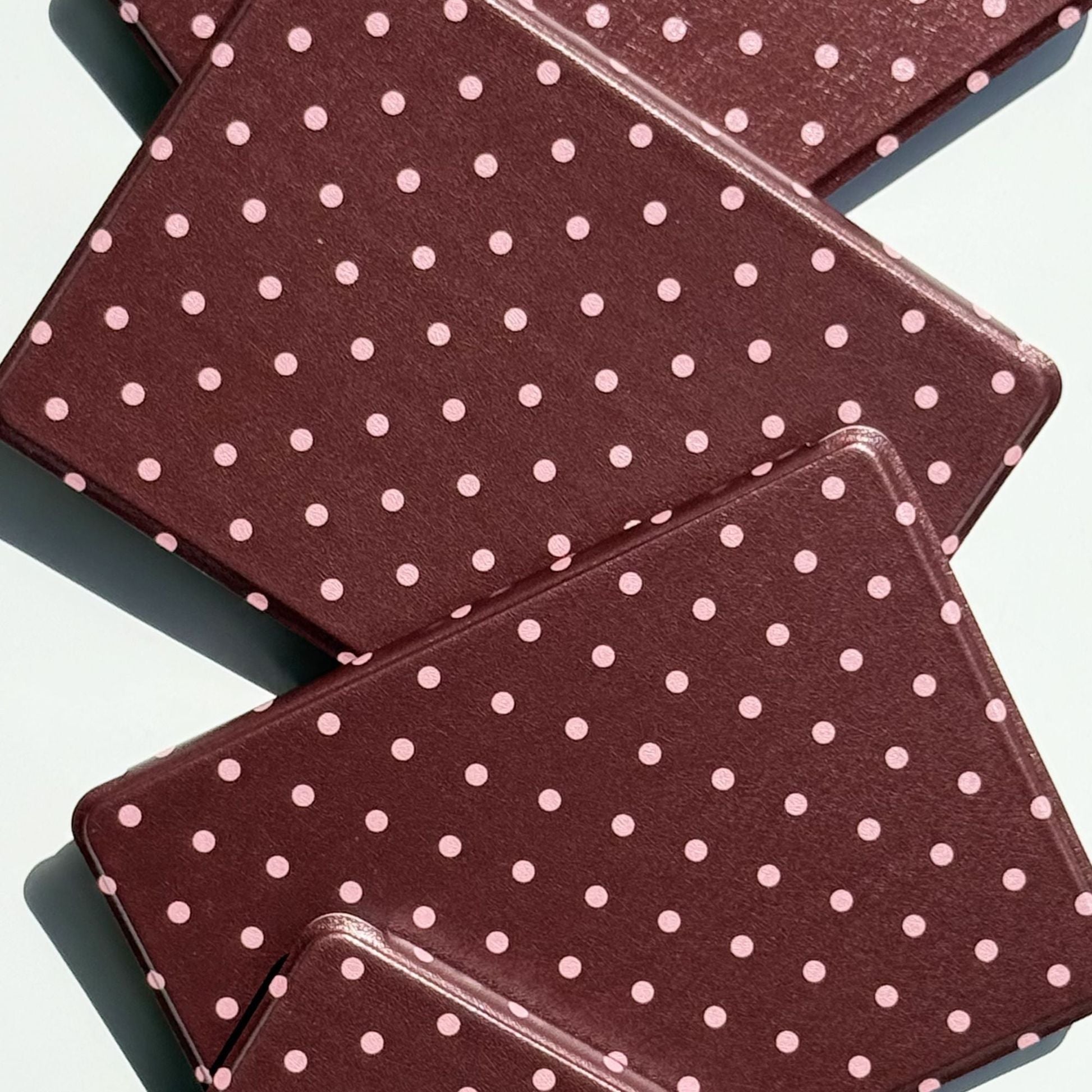 Close-up of overlapping Cocoa Kiss Kindle cases showing the soft pink polka dot print and slim profile