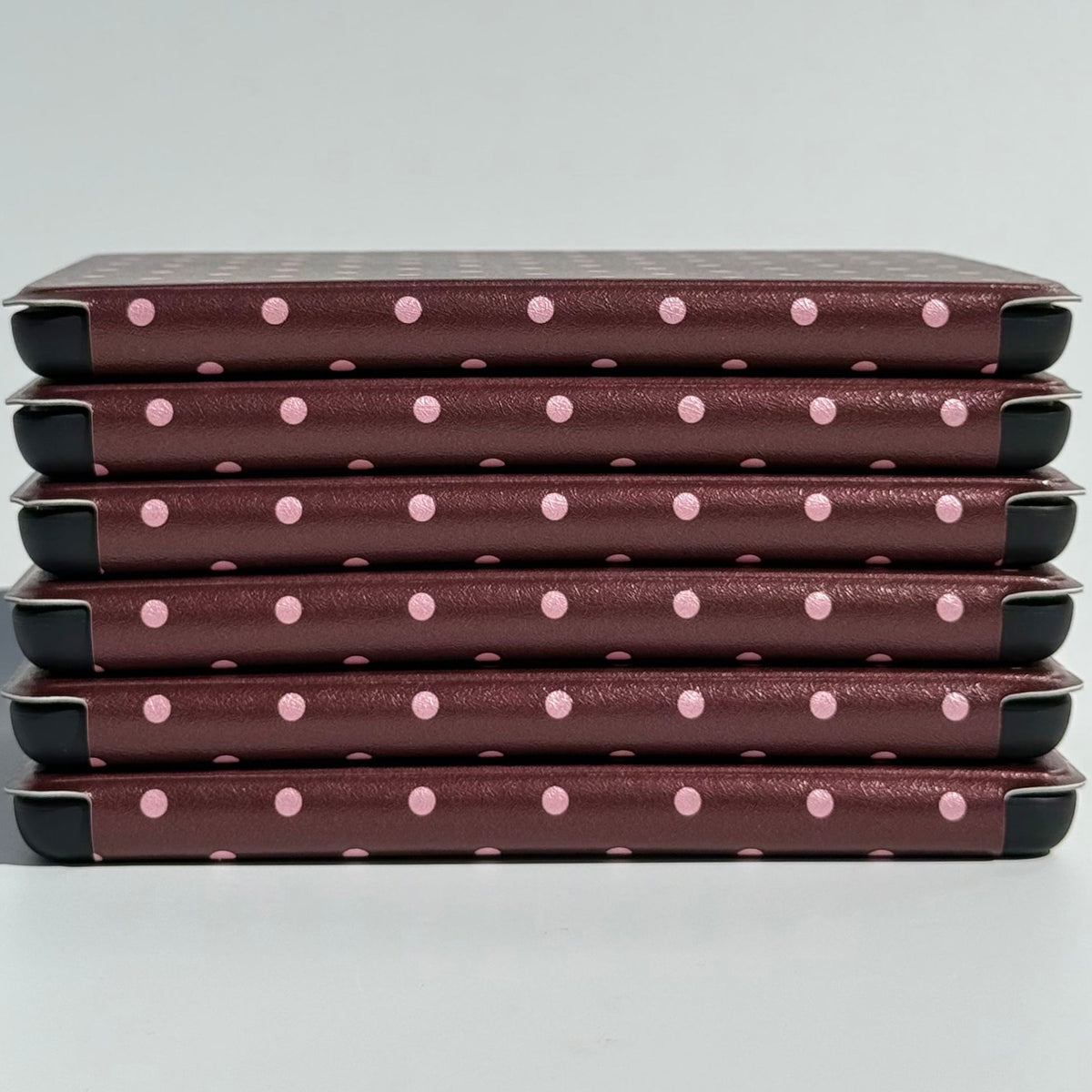 A stack of Cocoa Kiss Kindle cases from Case Society Australia, pink dots along every spine