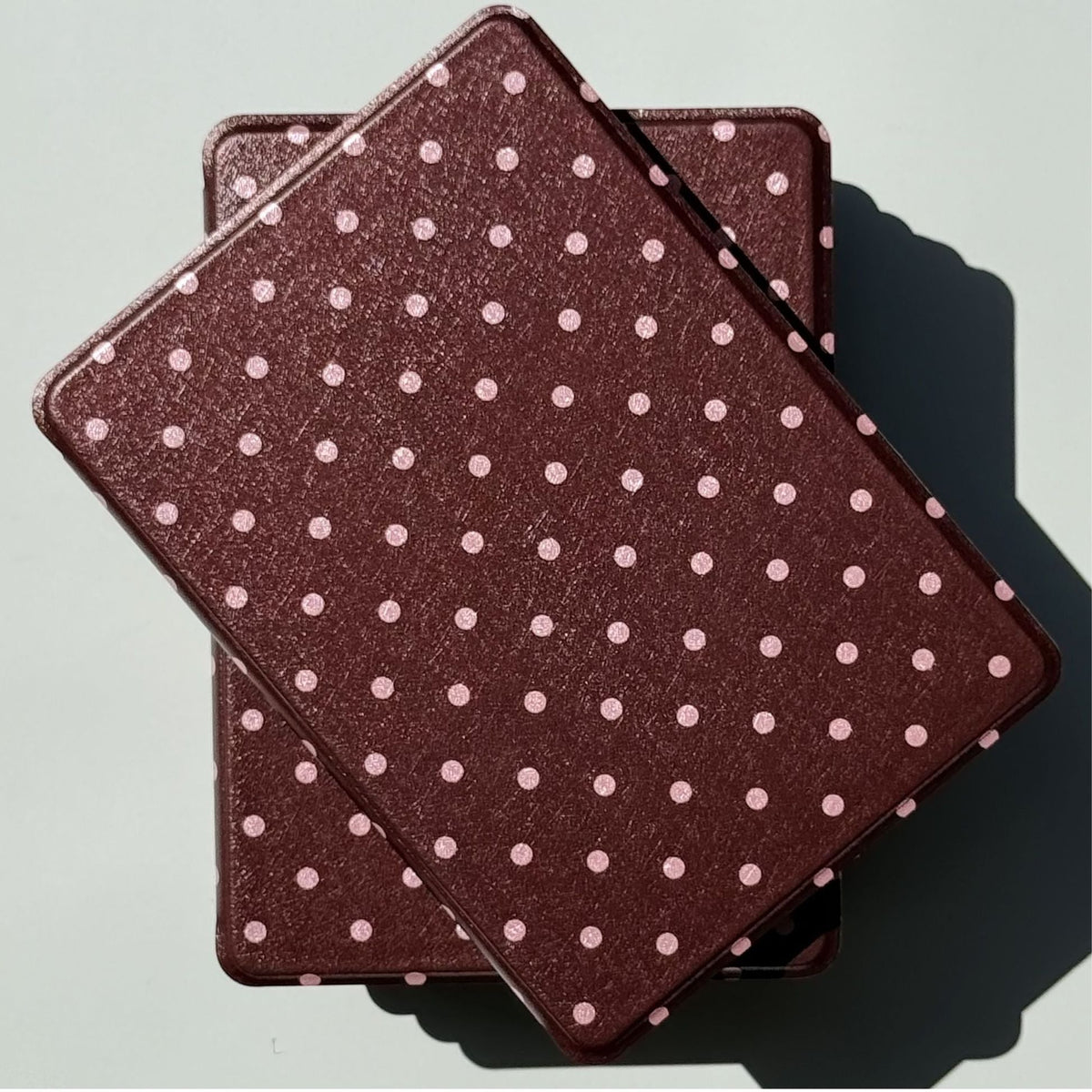 Two Cocoa Kiss Kindle cases stacked in bright sun, a chocolate and pink dot design from Case Society Australia