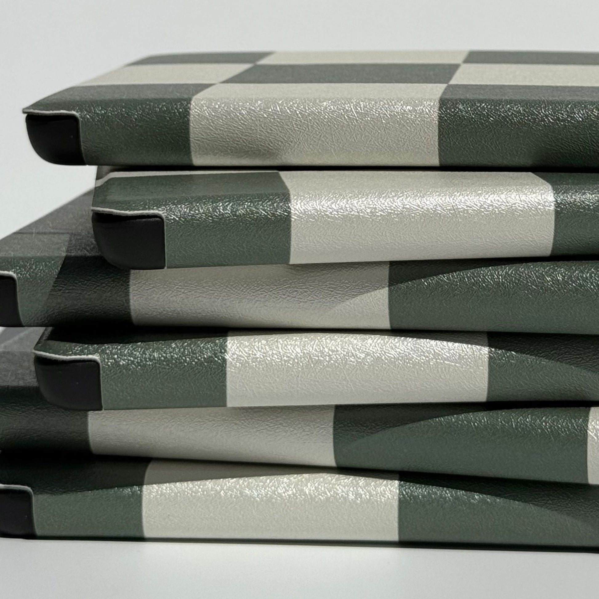 Stack of Forest Lore Kindle cases on edge showing green checkered print and reinforced corners 