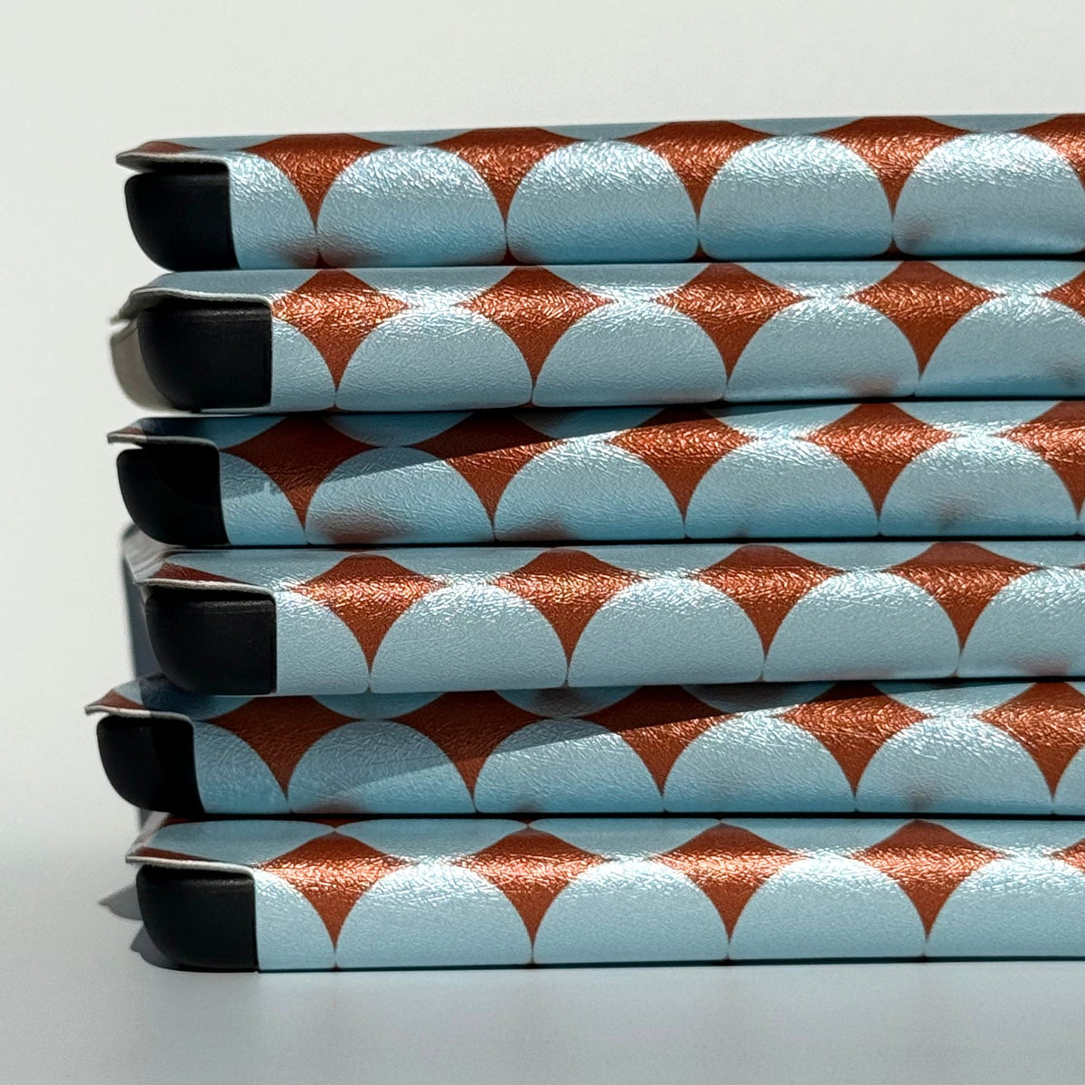 Scalloped spines of stacked blue polka dot Kindle cases with metallic copper diamonds