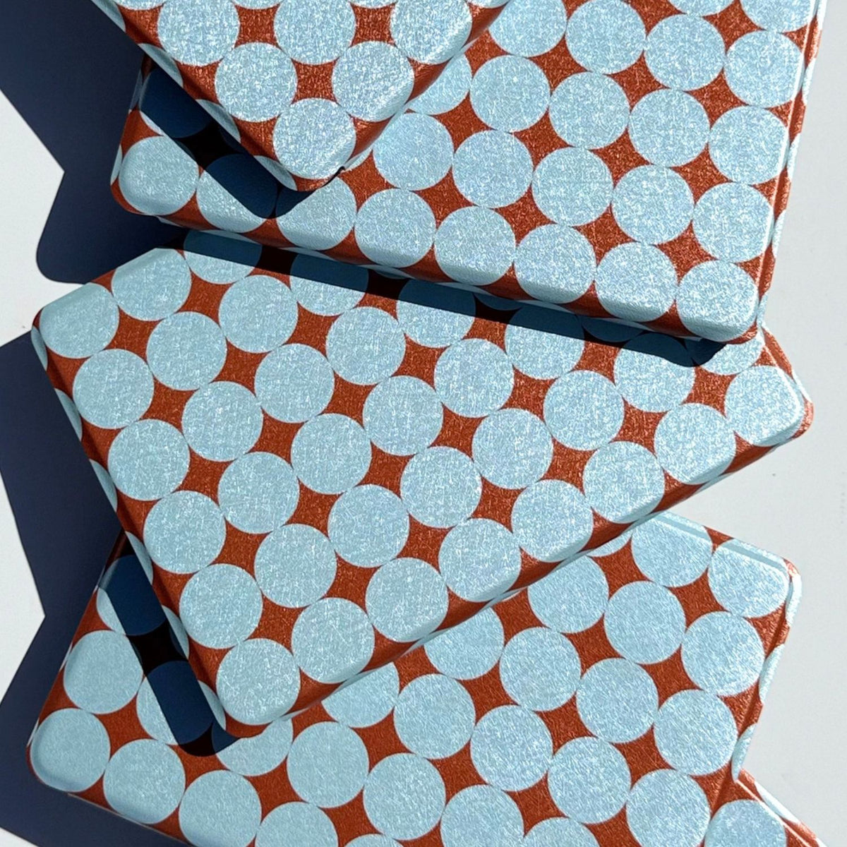 Three Meet Cute Kindle cases stacked in a zigzag, copper shimmer catching the afternoon sun