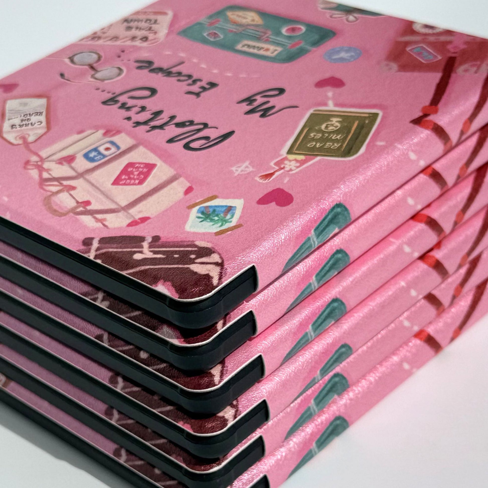 Top view of two Plotting My Escape Kobo Libra cases stacked, suitcase and book aesthetic on pink cover