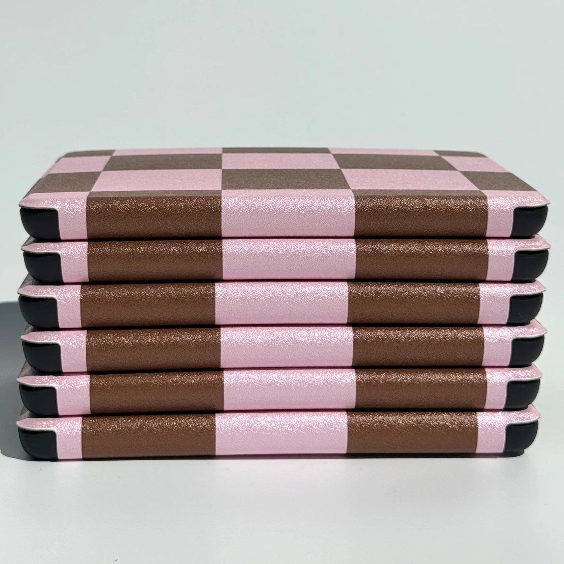 Angled flatlay of She's Checked In pink and brown checkerboard Kindle cases — Y2K aesthetic