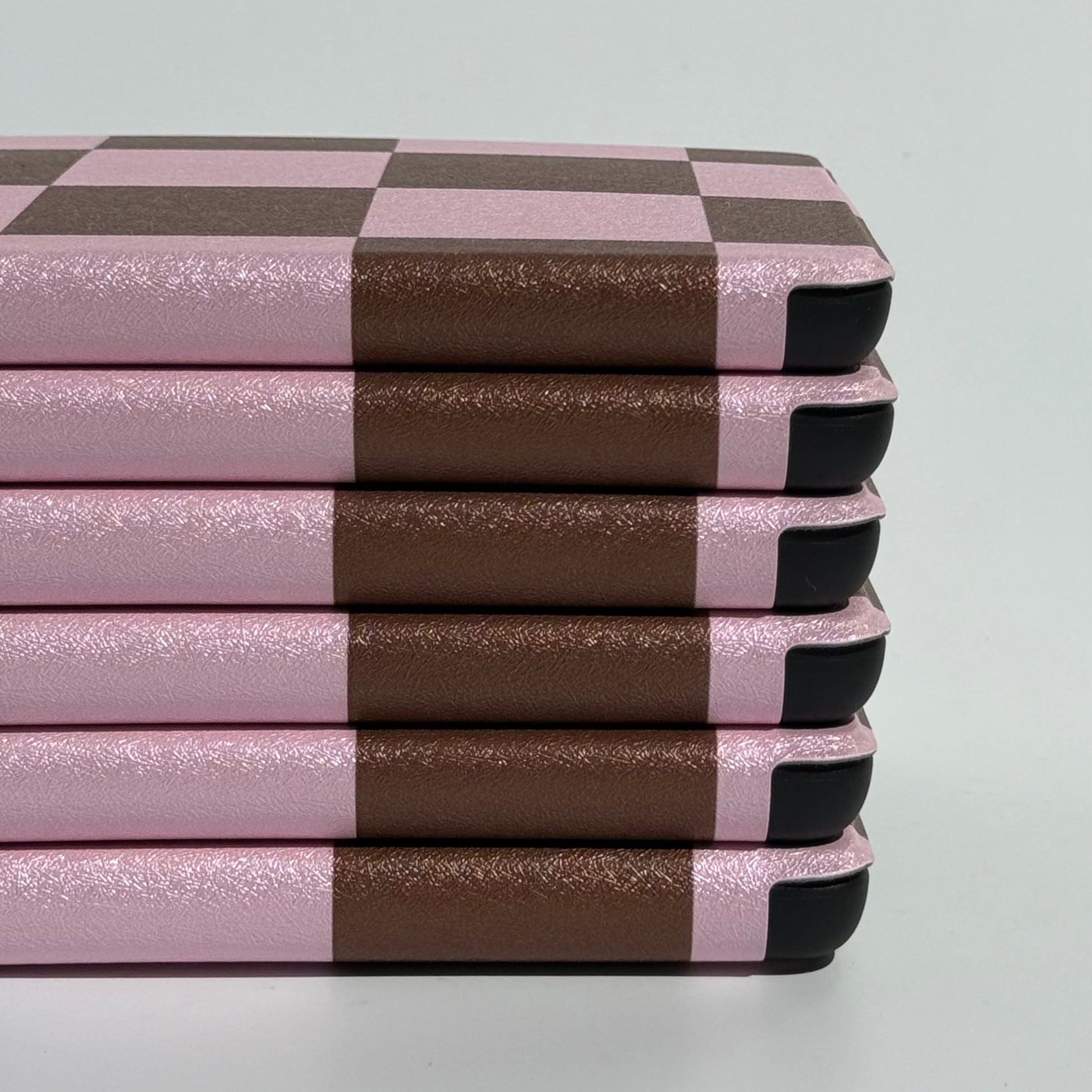 Neat stack of She's Checked In Kindle cases on edge showing pink and brown checkered edges and slim profile