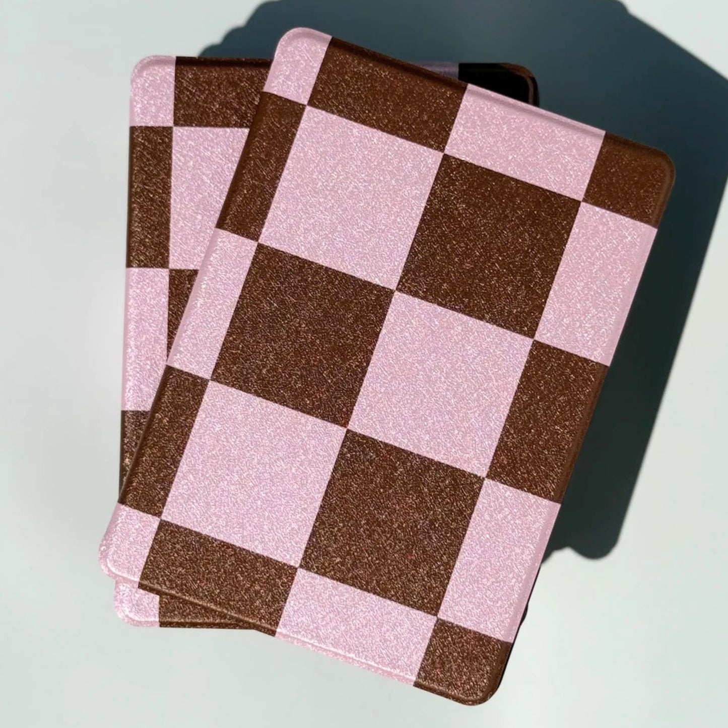 Stacked pile of She's Checked In pink and brown checkered Kindle cases — aesthetic bookish case AU