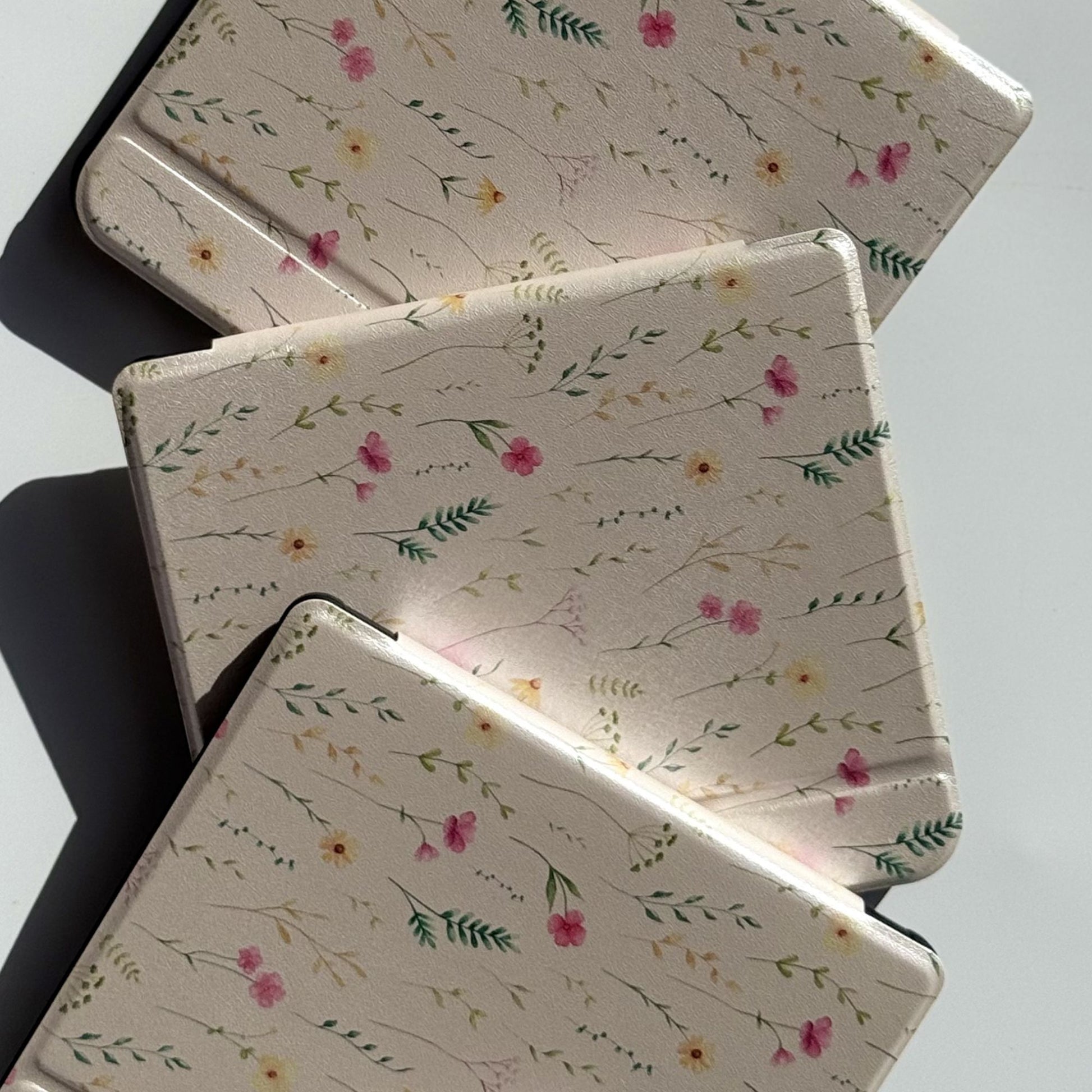 Flat lay of three Spring Court Kobo Libra cases in cream cottagecore floral print — delicate watercolour wildflowers and botanical sprigs