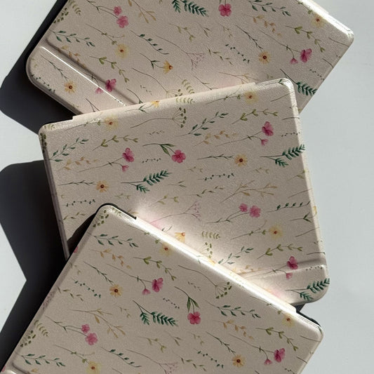 Flat lay of three Spring Court Kobo Libra cases in cream cottagecore floral print — delicate watercolour wildflowers and botanical sprigs