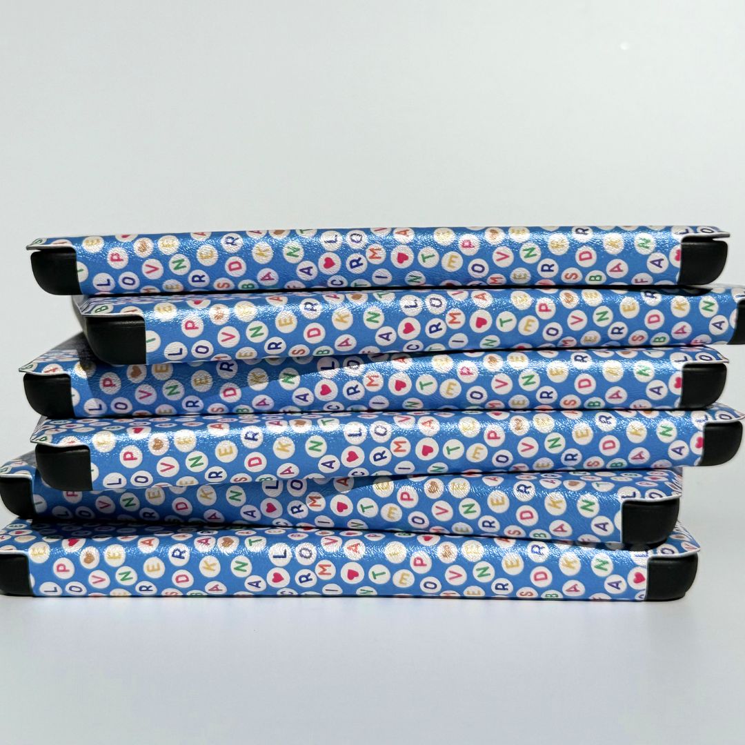 Stack of Swiftly Written Kindle cases in blue with colourful letter bead print