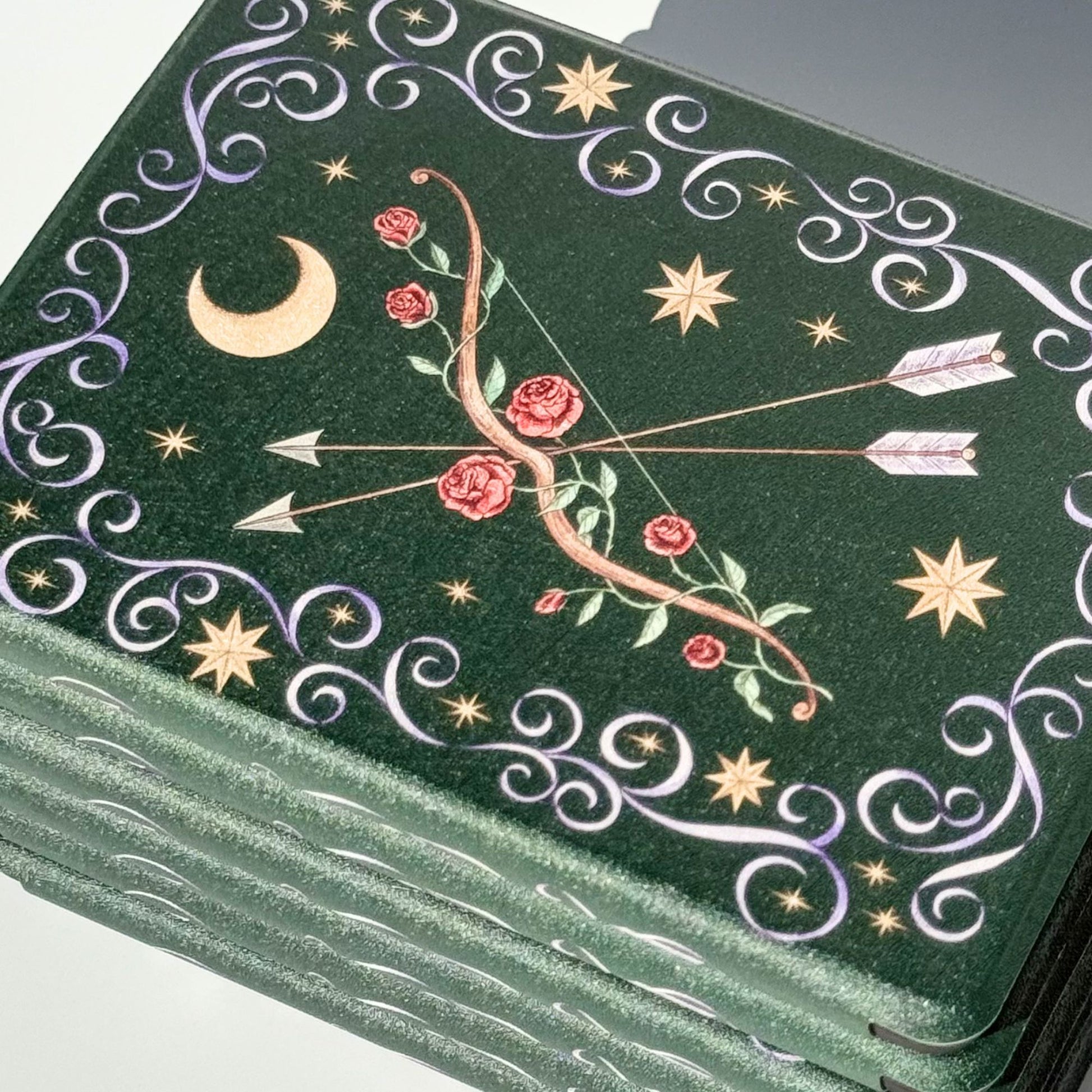 Angled stack of The Huntress Kindle cases, emerald green with rose bow and gold moon
