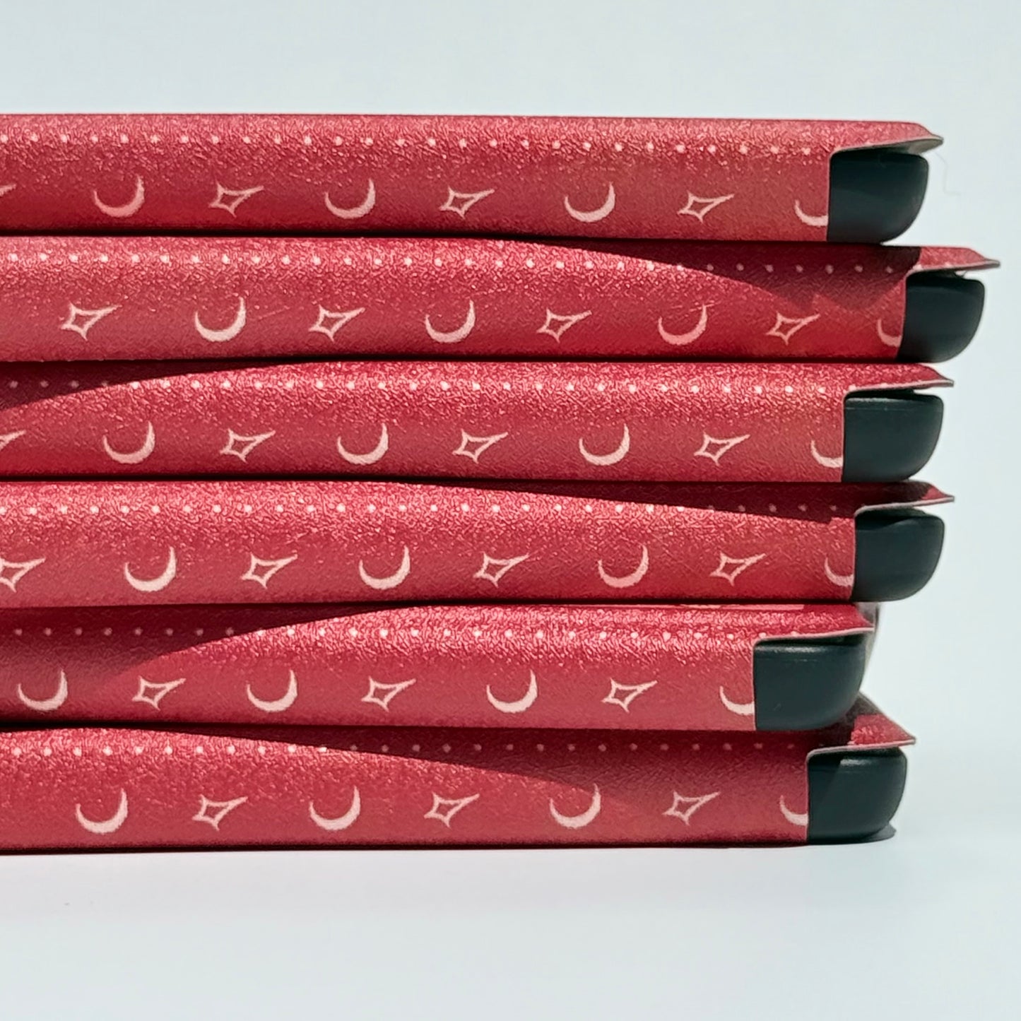 Side stack of The Lovers Kindle cases showing the gold crescent-moon pattern along the spine — Case Society AU