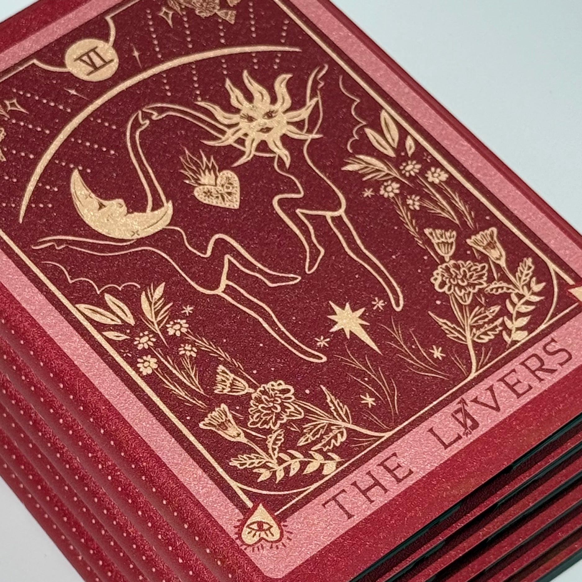 Flat overhead stack of The Lovers Kindle cases showing red spine edges with a repeating gold moon motif