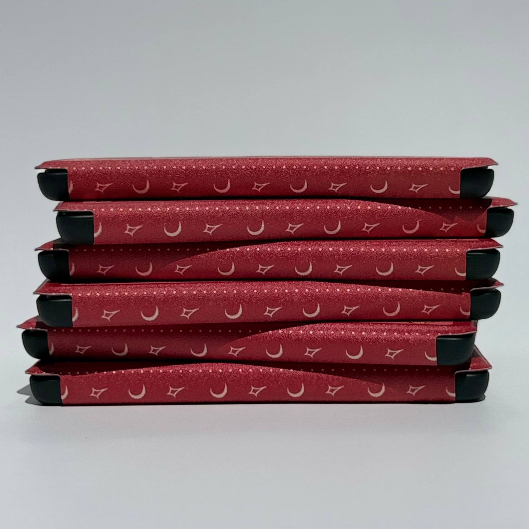 Stack of The Lovers wine red Kindle cases showing the black hand straps for one-handed reading