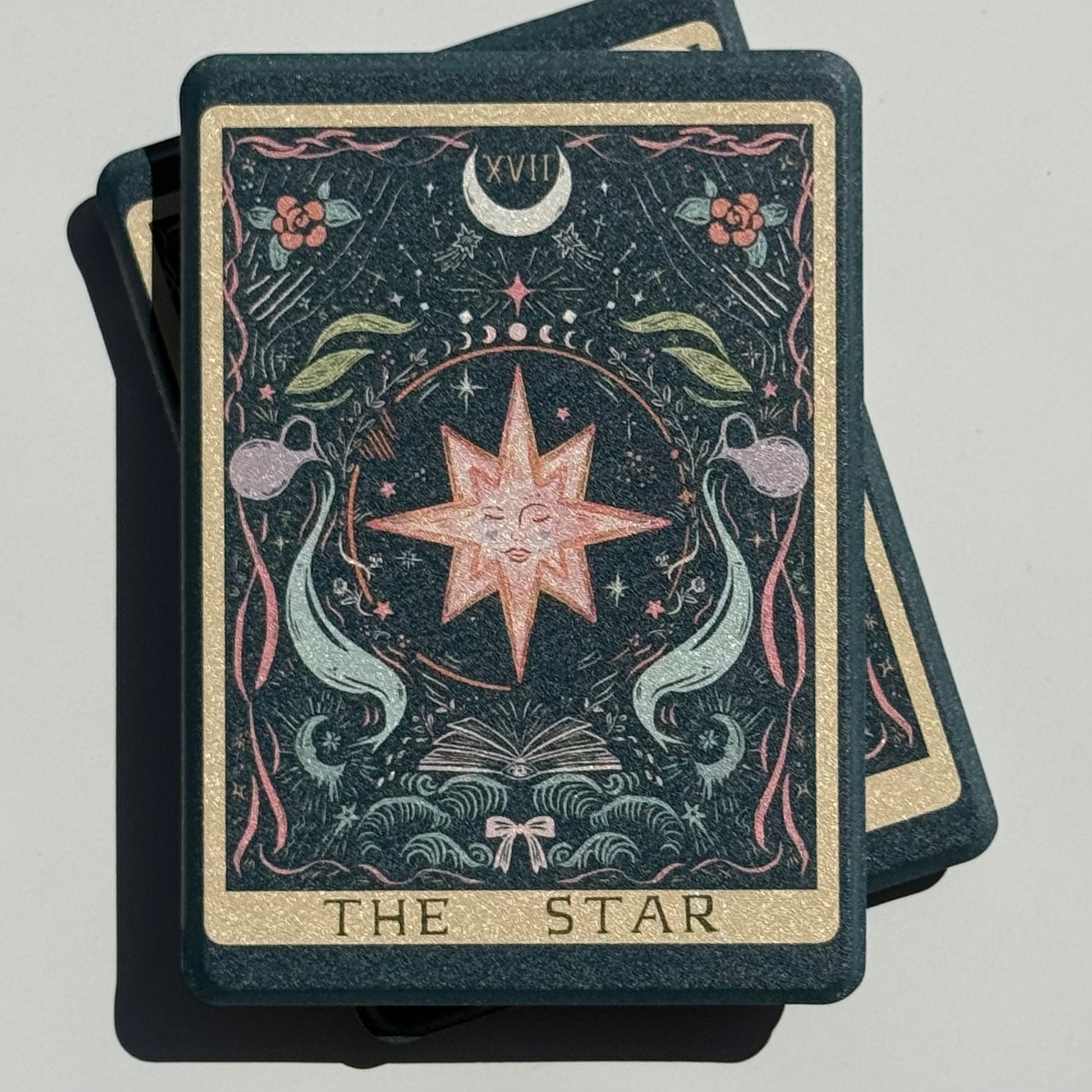 Sunlit stack of The Star Kindle cases, the full card XVII illustration with THE STAR lettering in gold