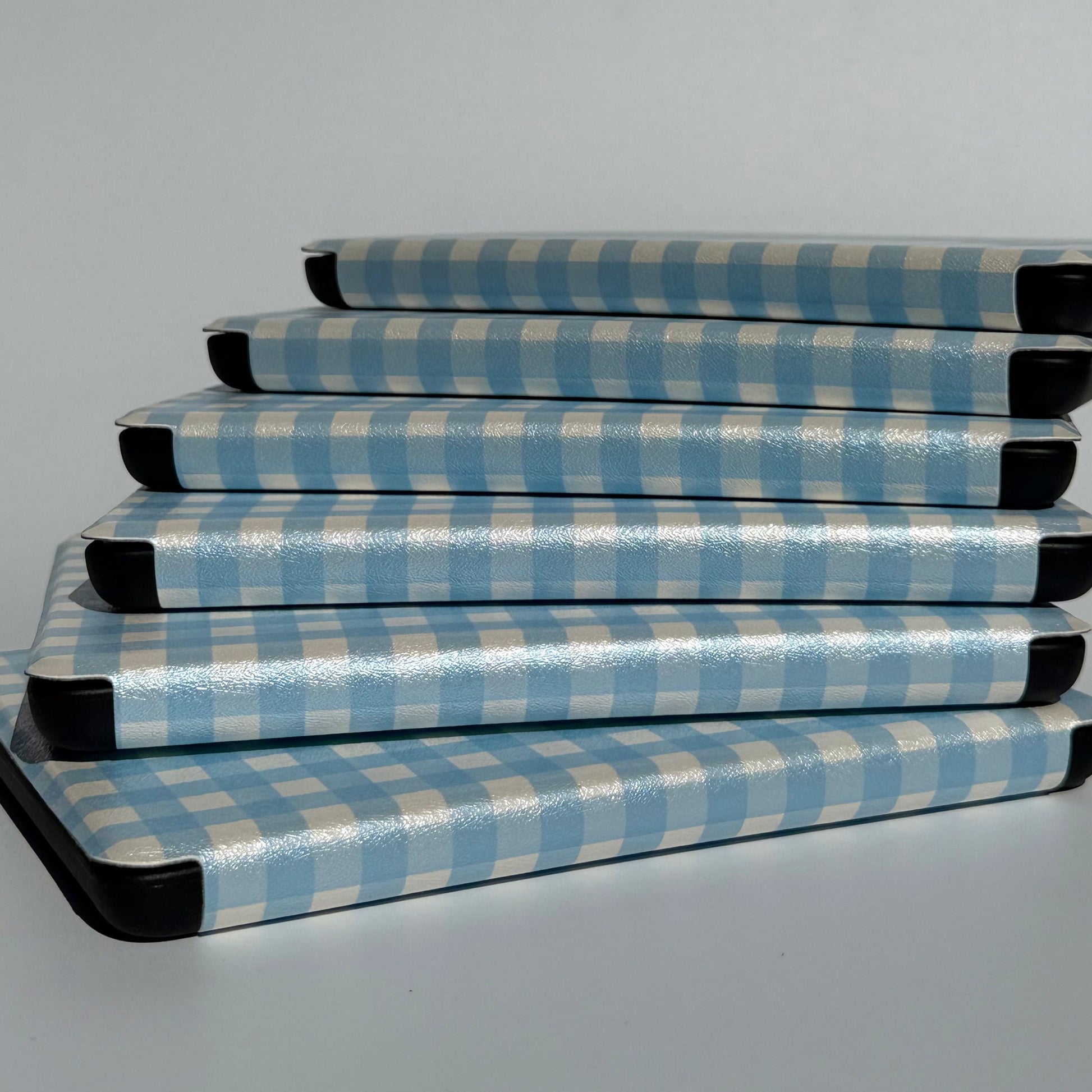 Stack of The Quiet Blue Kindle cases on edge showing blue gingham print and protective black spine