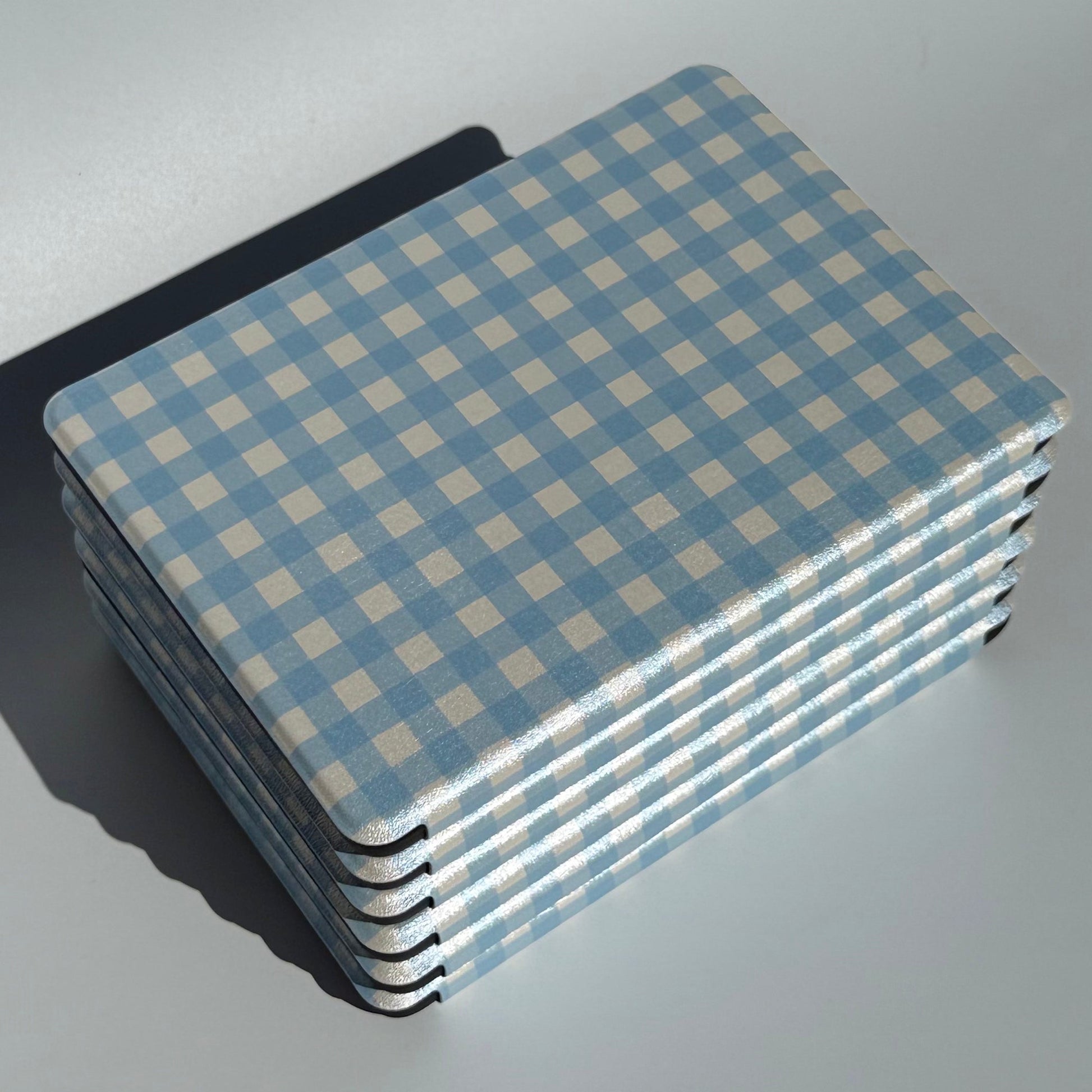 Angled stack of The Quiet Blue blue gingham Kindle cases highlighting slim profile and reinforced corners