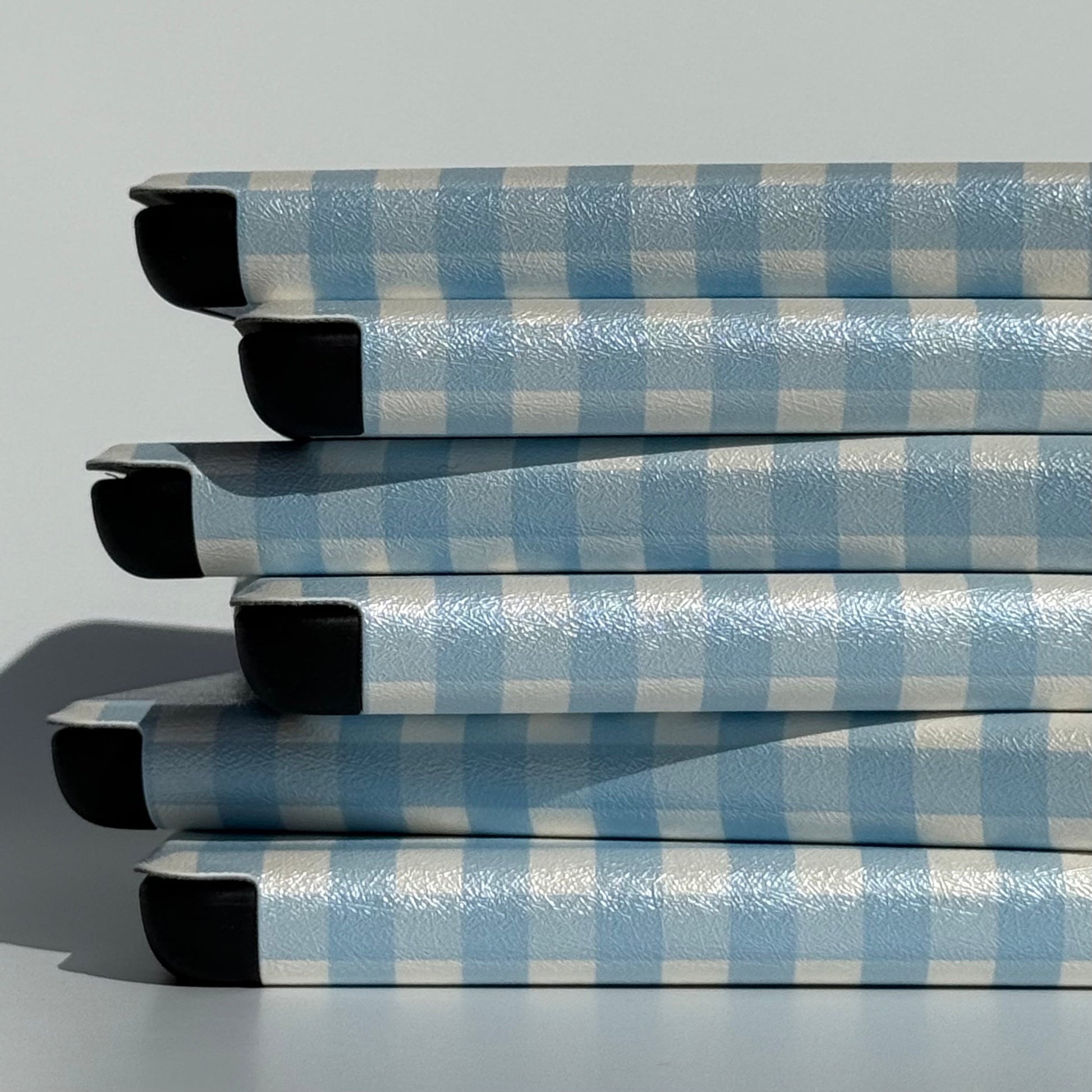 Stack of The Quiet Blue blue gingham Kindle cases with shockproof shell