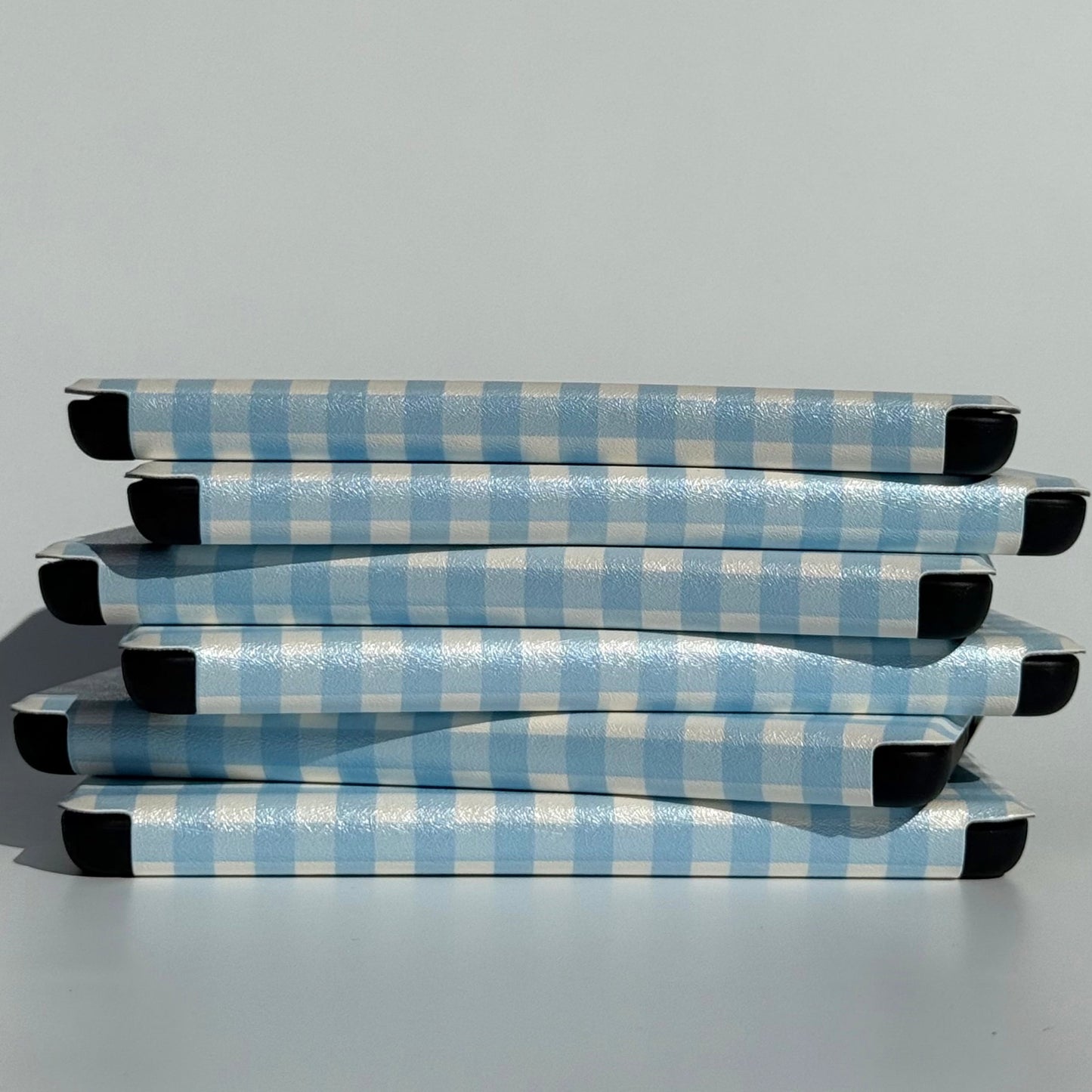 Stack of The Quiet Blue blue gingham Kindle cases with hand strap and magnets