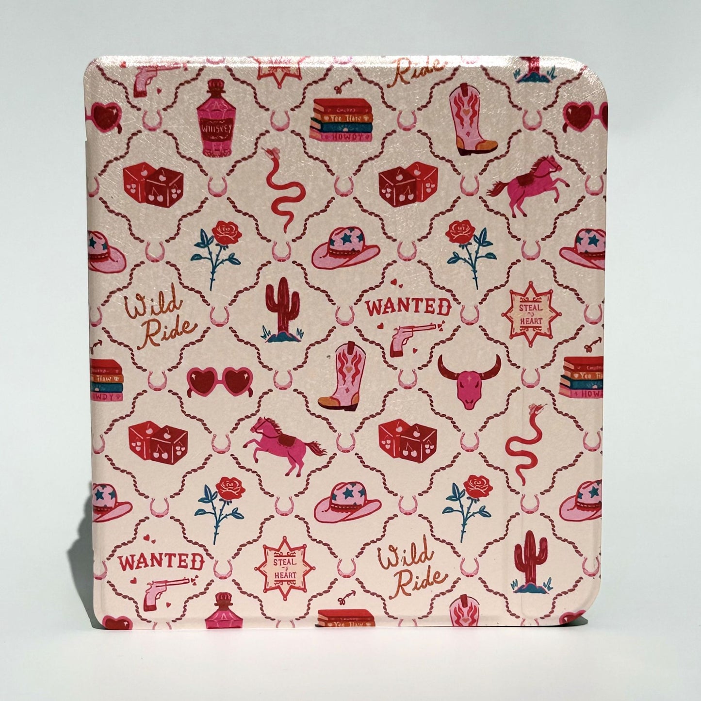 Overlapping flat lay of Wild Ride Kobo Libra cases showing pink cowboy hats, boots, horses, dice, books and roses on cream pink background